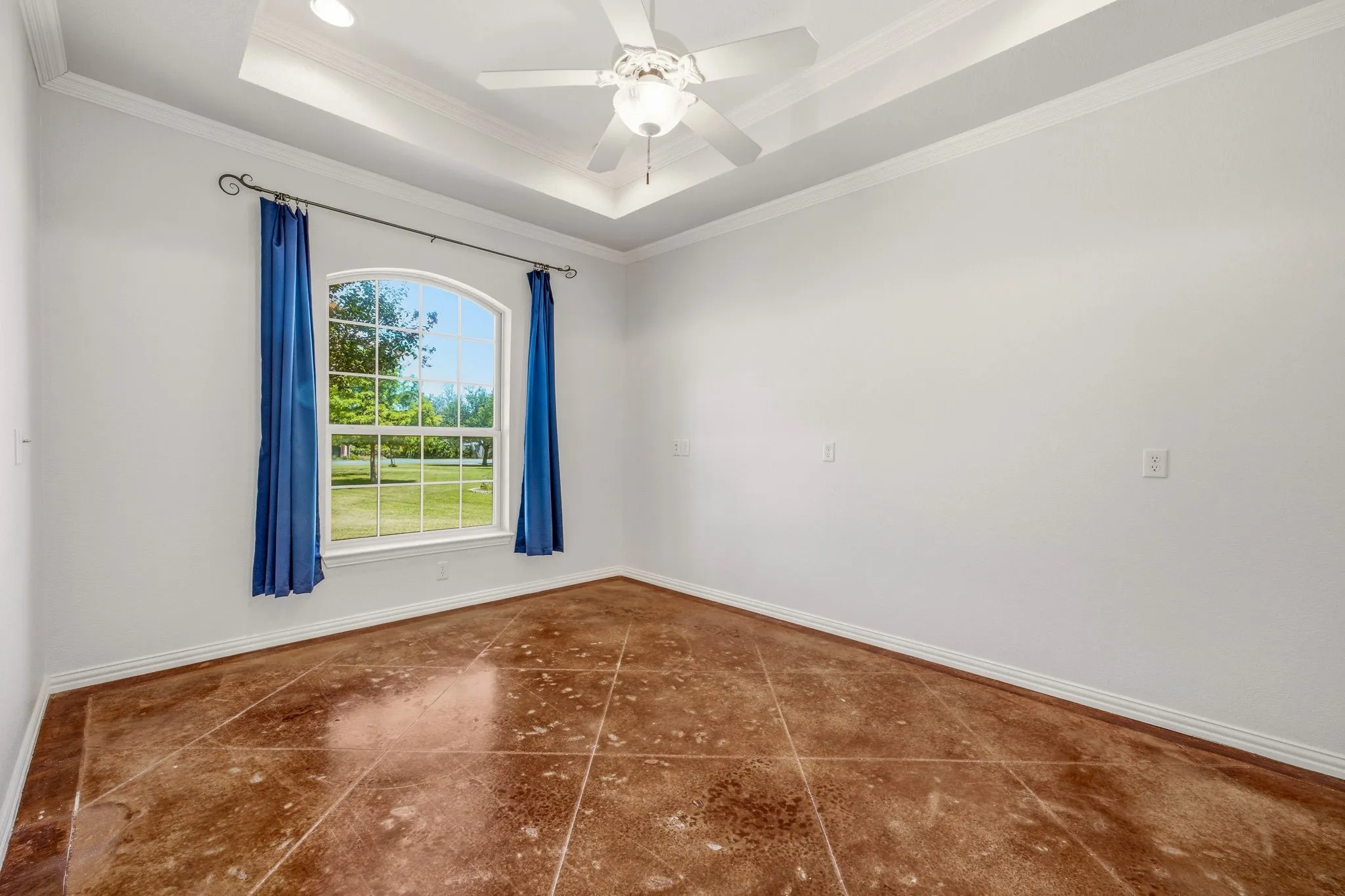 Room featuring a tray ceiling with a ceiling fan, an arched window, white walls, and decorative tile flooring