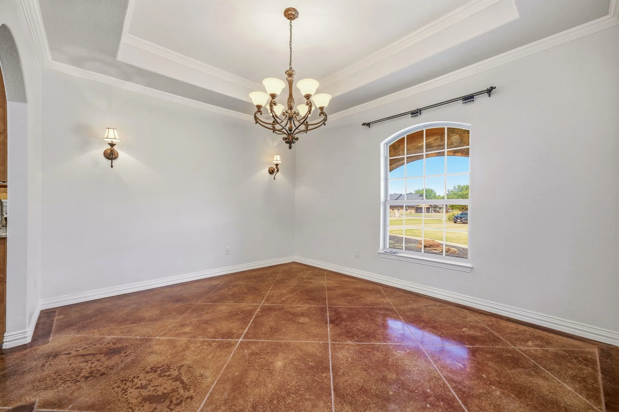 Spacious room featuring a tiered tray ceiling, arched window with grid details, a bronze chandelier, and coordinating wall sconces