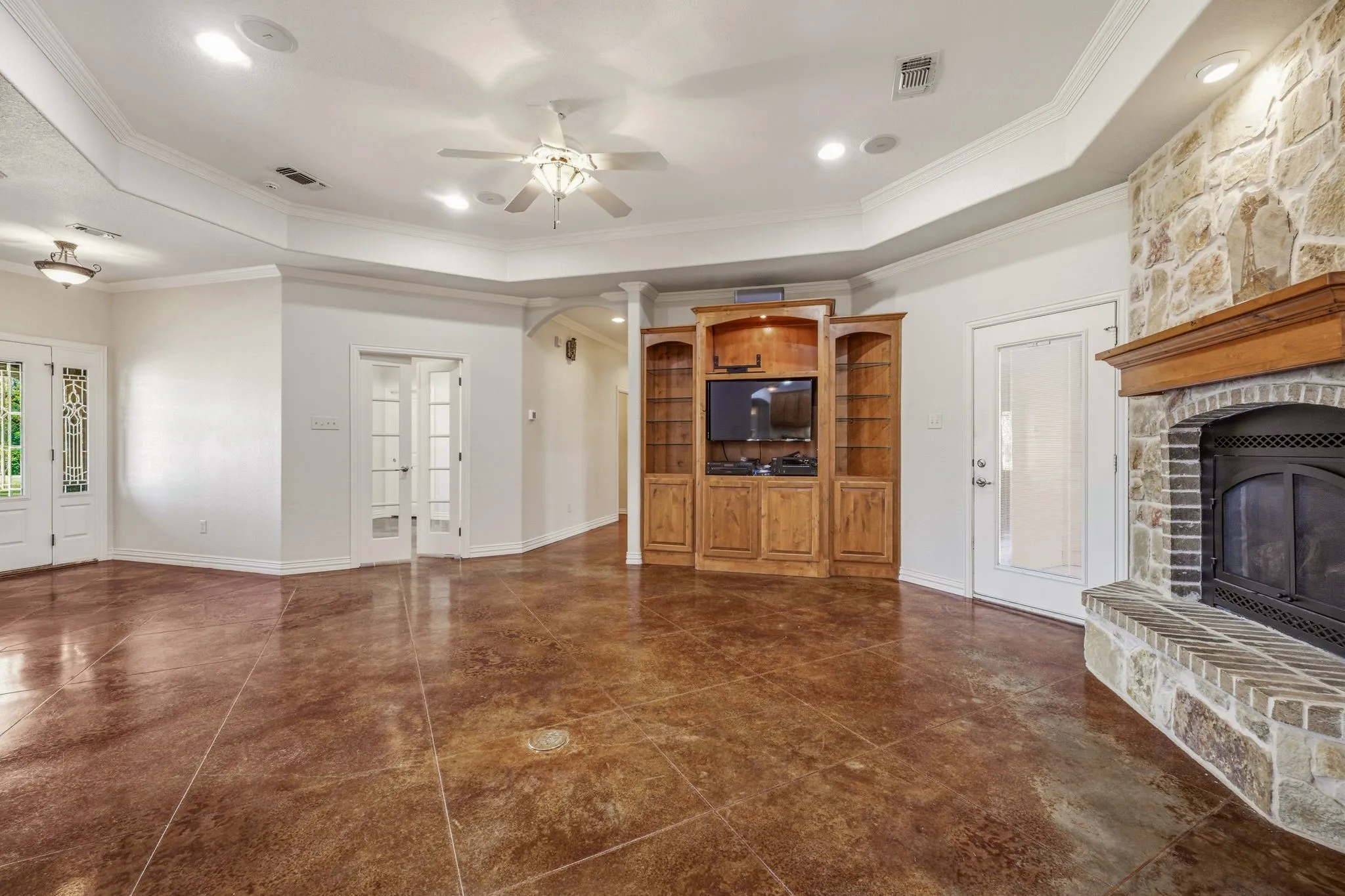 Spacious living area featuring polished concrete flooring, a stone fireplace with a wood mantel, a built-in entertainment center, coffered ceilings, and recessed lighting
