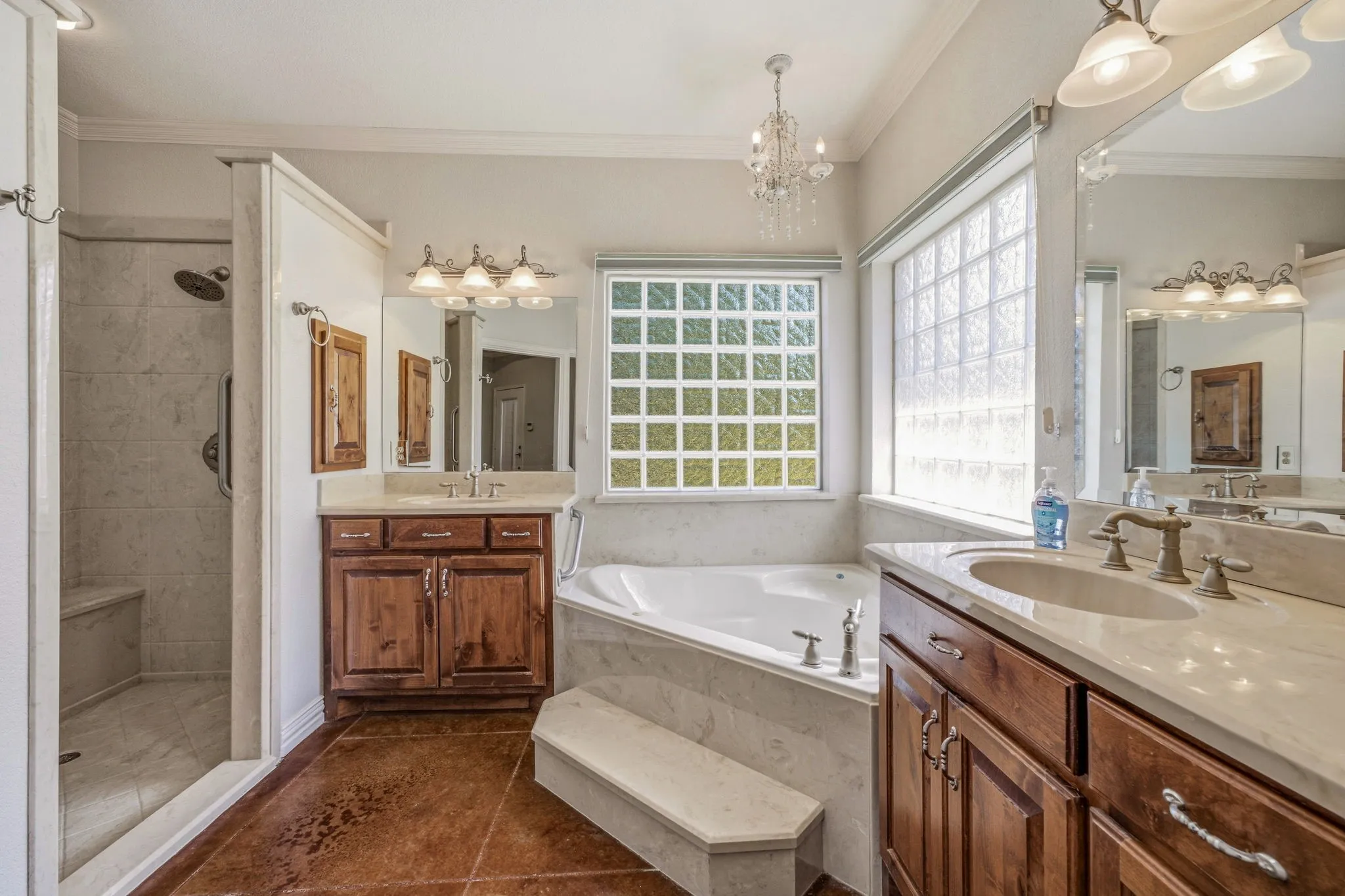 Bathroom featuring a corner soaking tub with marble surround, double vanities with stone countertops, wood cabinetry, and a walk-in shower with a built-in bench