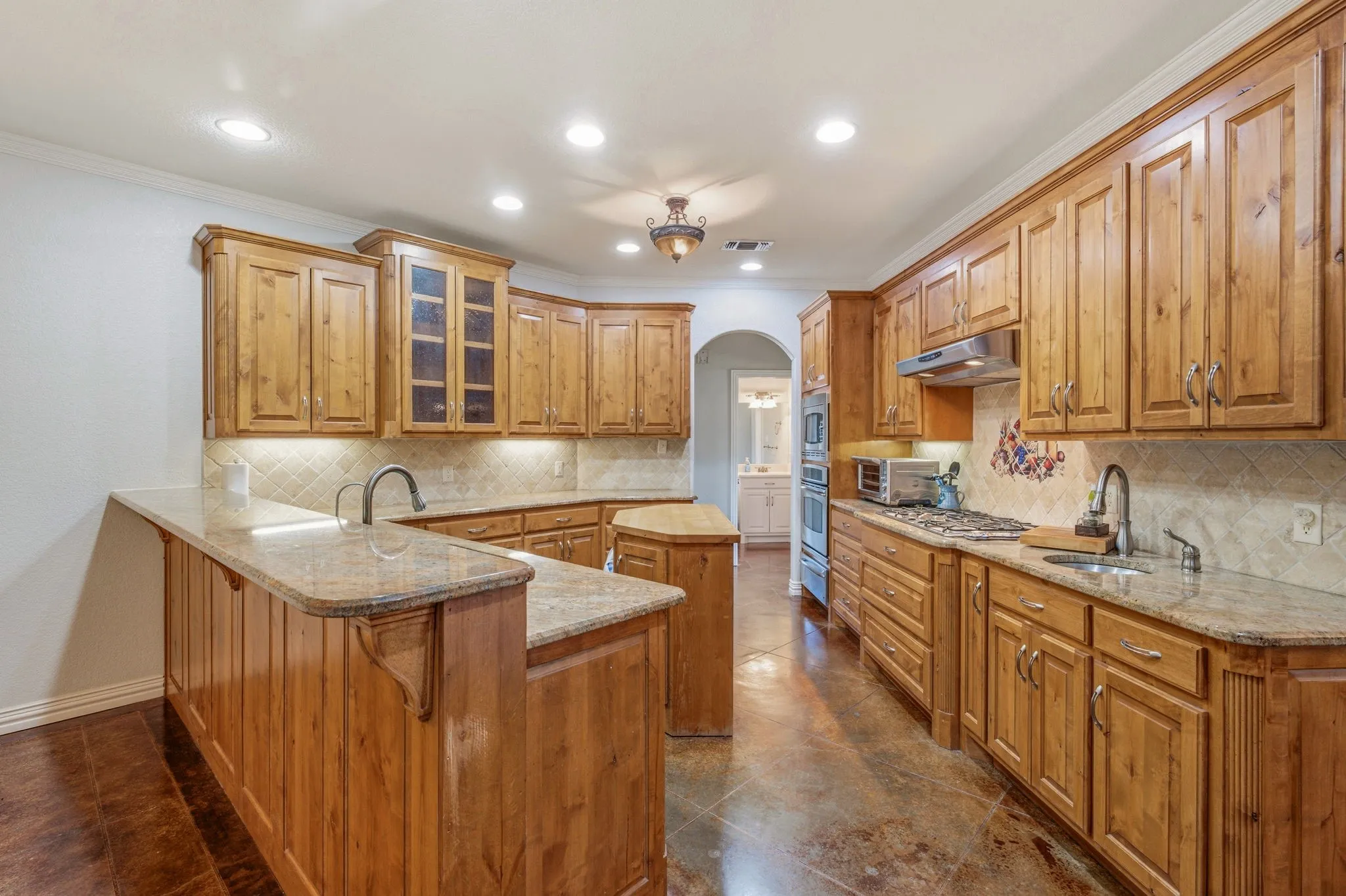 Expansive kitchen with abundant wood cabinetry, granite countertops, tile backsplash, stainless steel appliances, and integrated recessed lighting