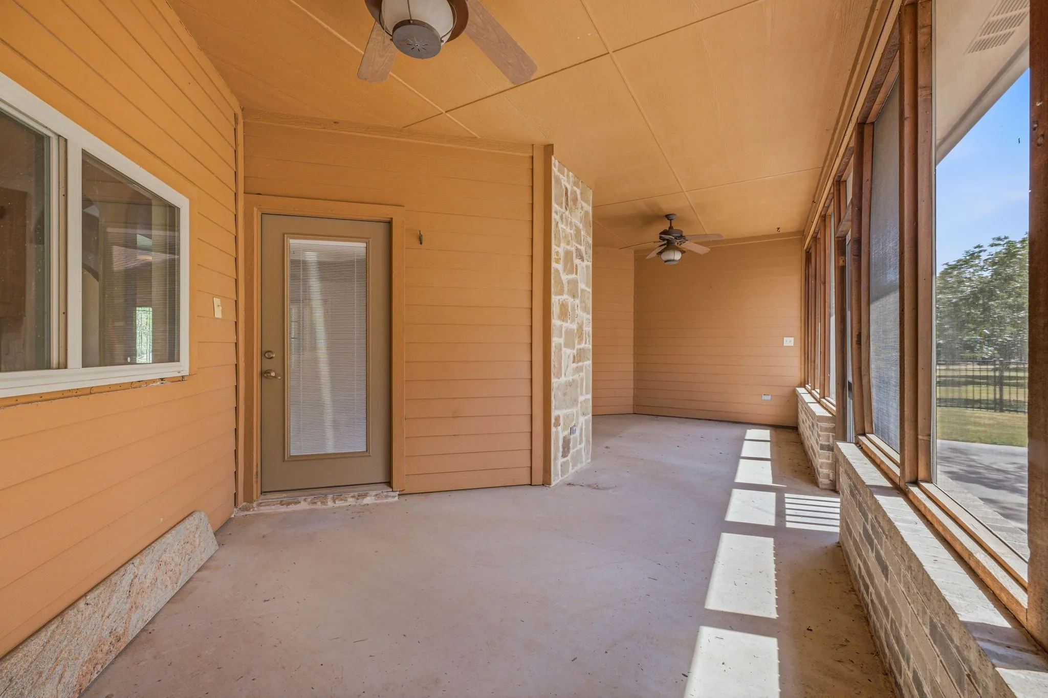Screened porch featuring a concrete floor, stone accent walls, multiple ceiling fans, and clear exterior views