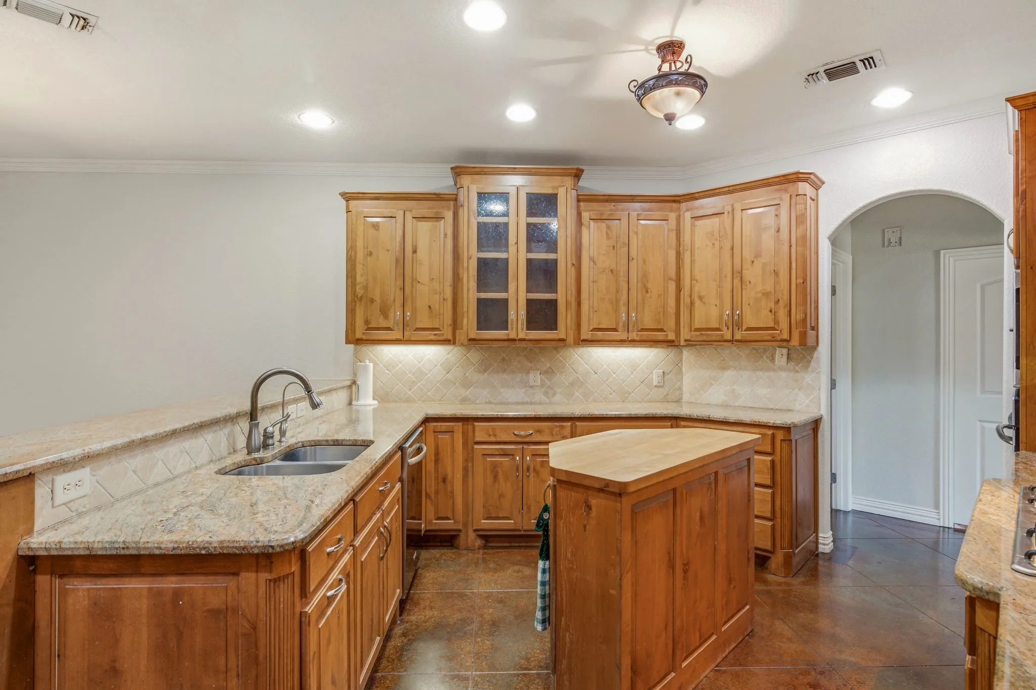 Kitchen featuring wood cabinetry, granite countertops, a double basin sink, and a central island with a butcher block top