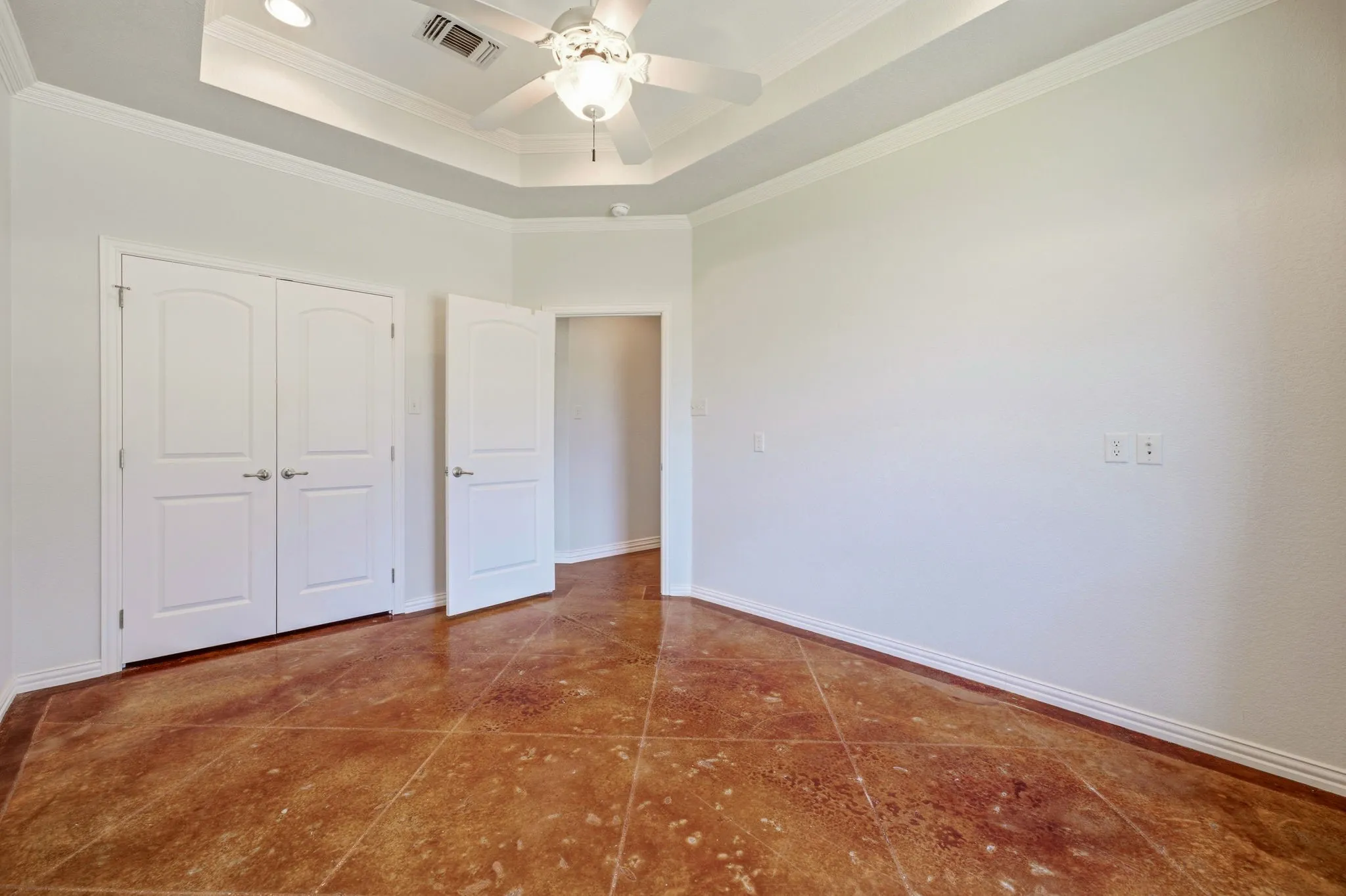 Spacious room featuring rich, textured floor tiles, a tray ceiling with recessed lighting, and a ceiling fan