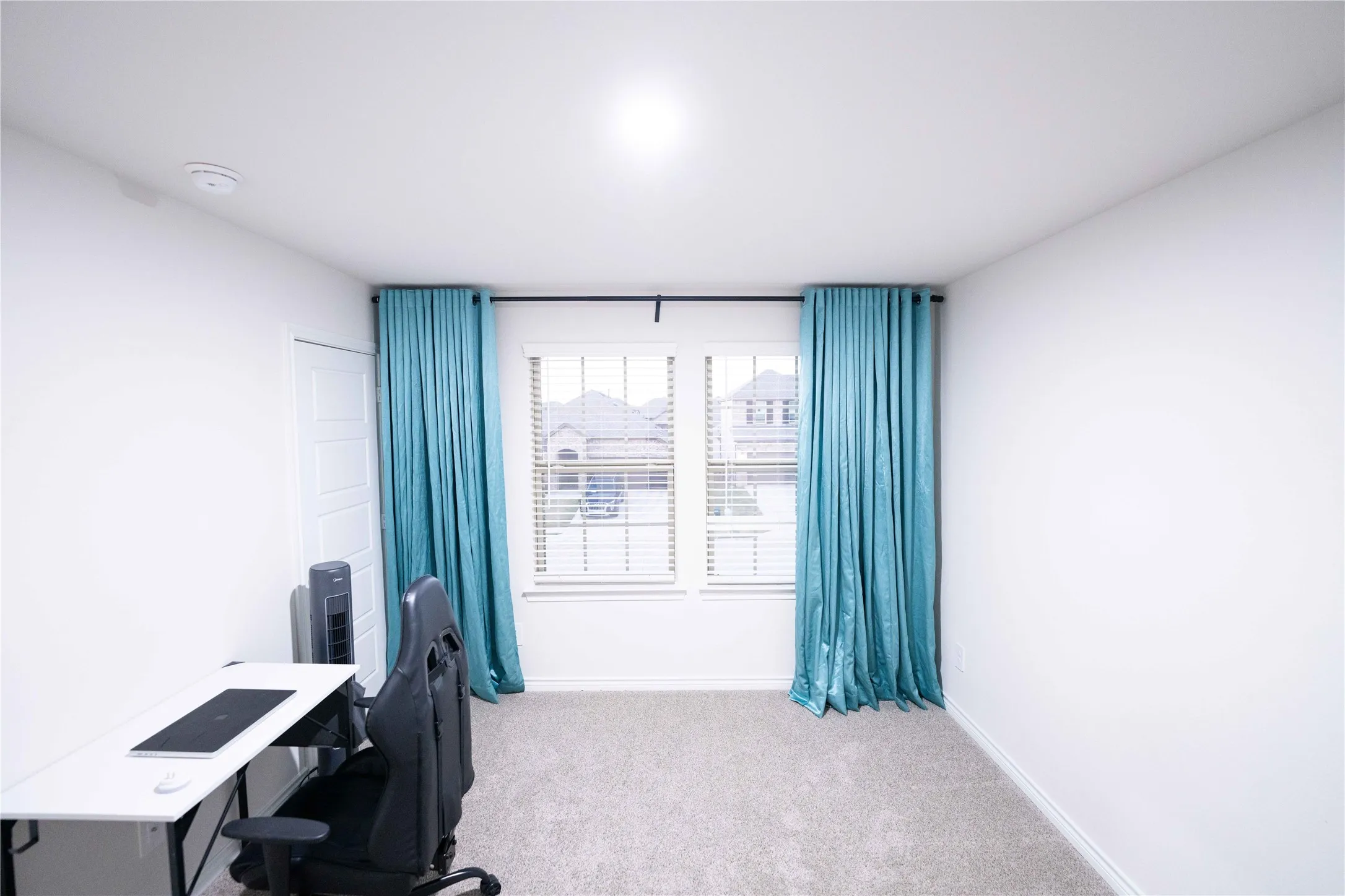 Carpeted room featuring two windows with blinds, a white paneled door, and white walls