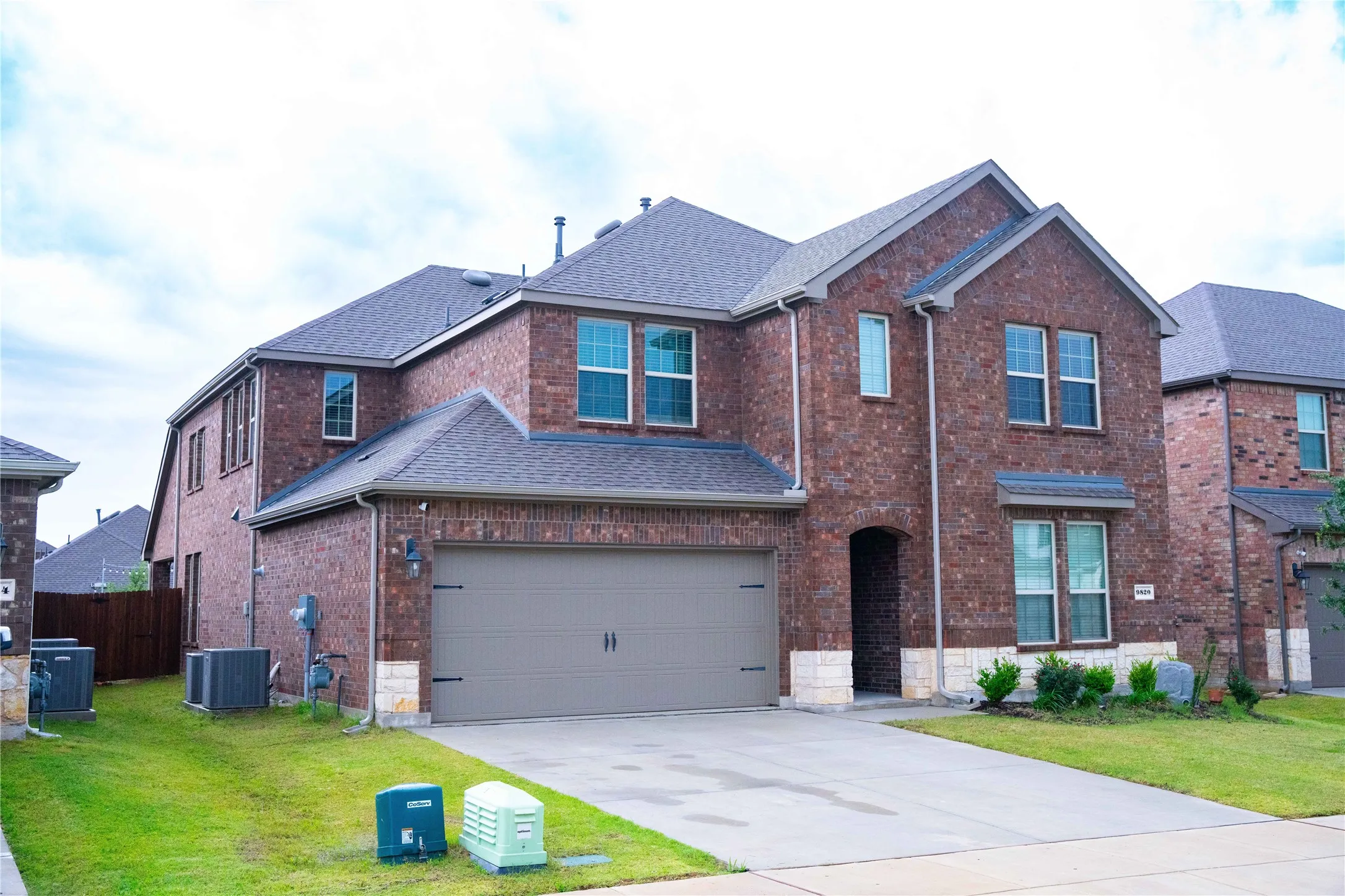 Two-story brick exterior with stone accents, a gray asphalt shingle roof, a two-car garage, an arched entry, and a concrete driveway