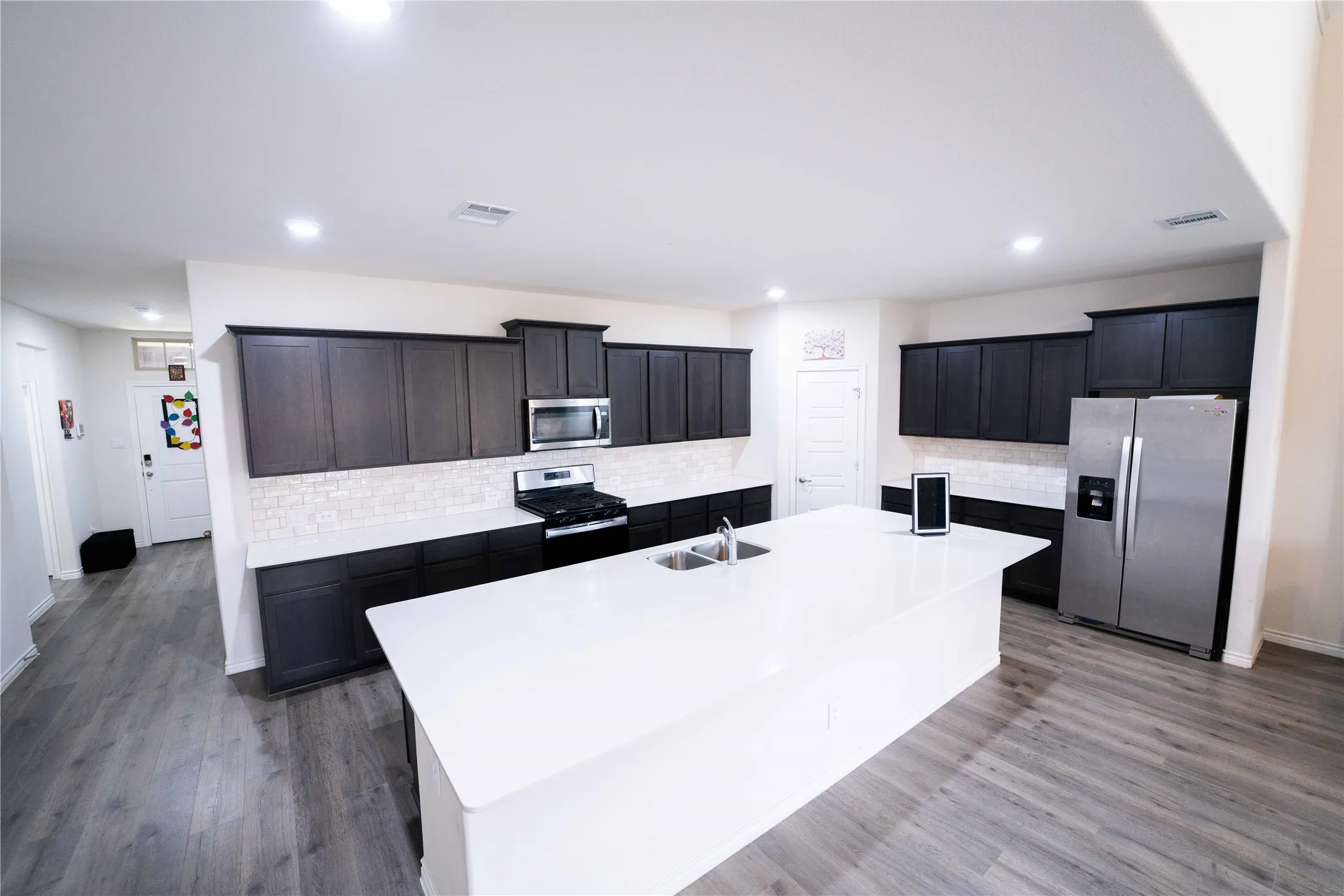 Kitchen featuring an expansive center island with an integrated sink, dark wood-finish cabinetry, stainless steel appliances, a white subway tile backsplash, and wood-finish flooring