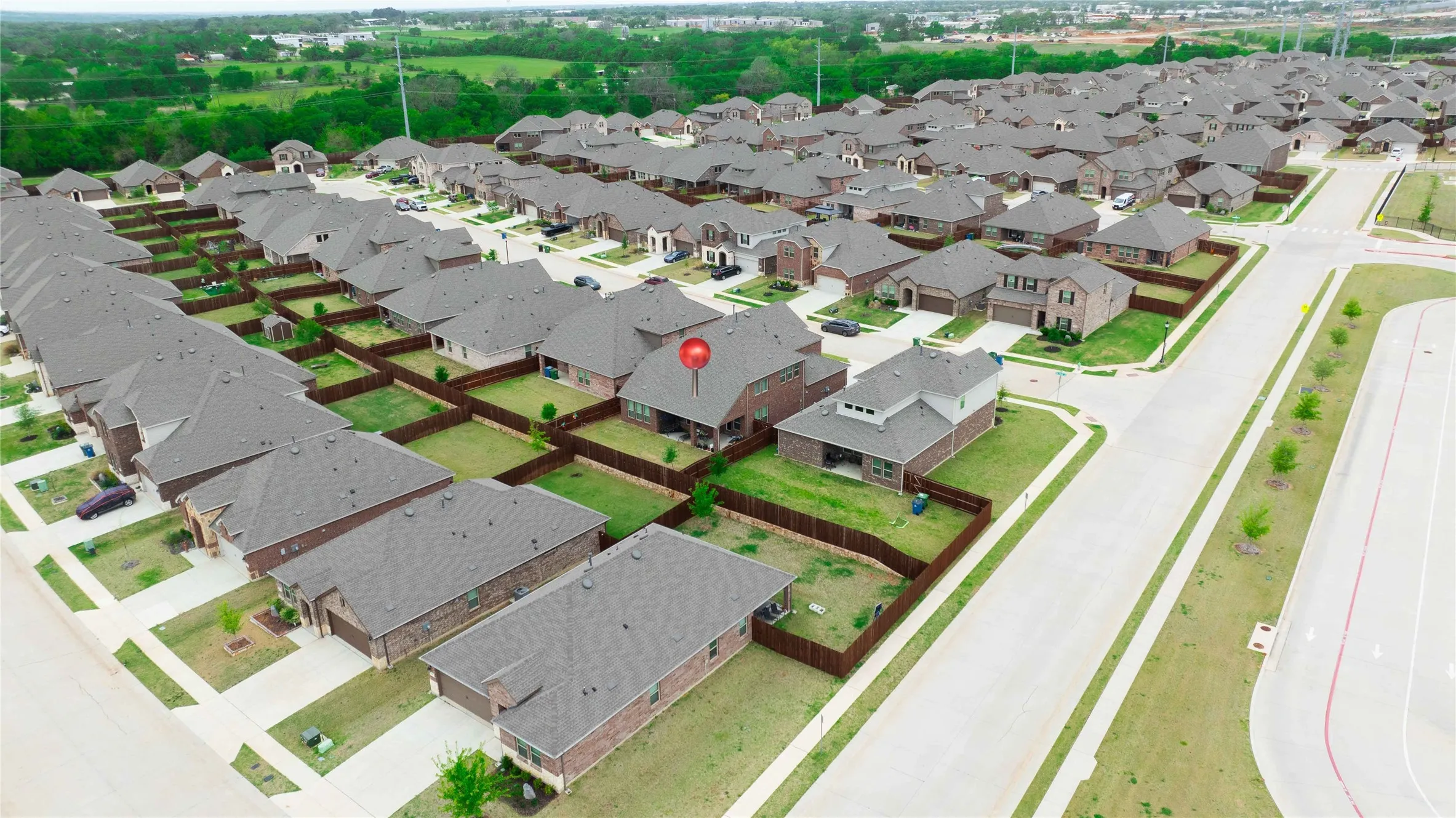 Residential development featuring single-family homes with brick and siding exteriors, dark shingle roofs, and fenced backyards
