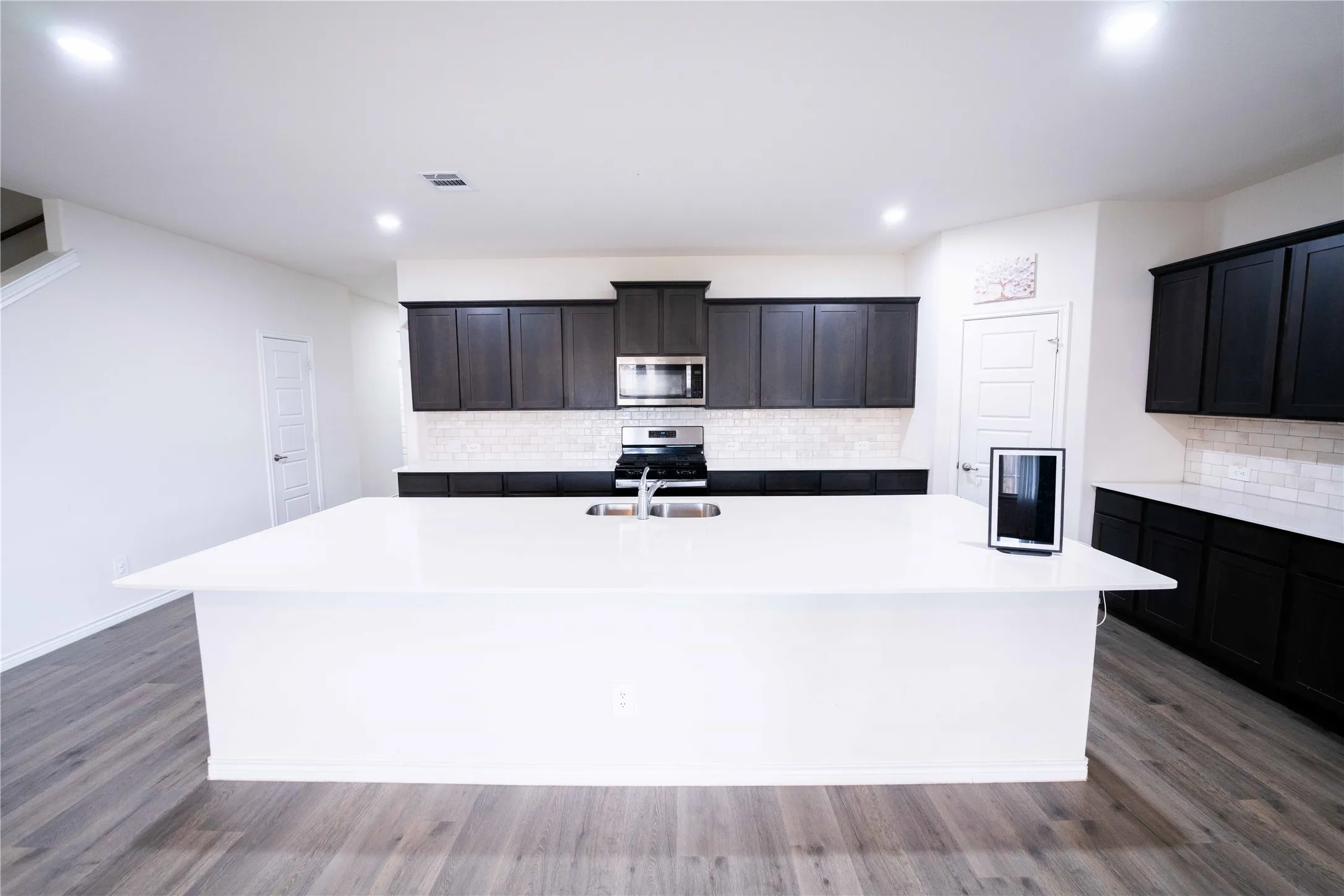 Expansive kitchen island with white countertop, dark wood-finish cabinetry, stainless steel appliances, and white subway tile backsplash