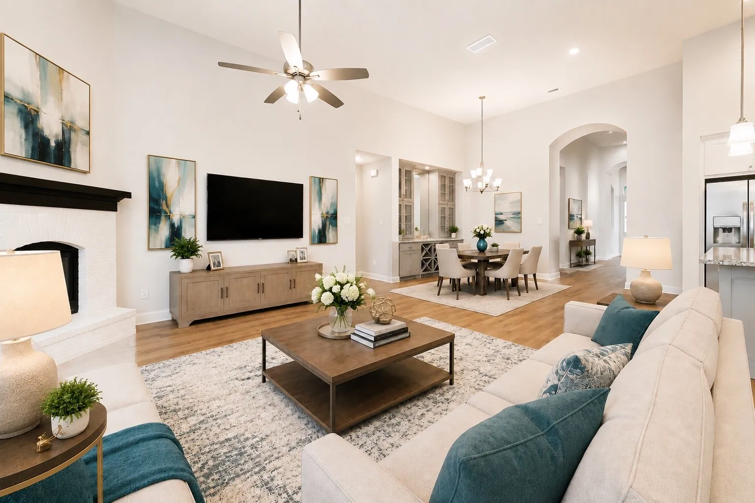 Vaulted ceilings accentuate this open-concept living area featuring wood-finish flooring, a white brick fireplace with a dark mantel, and a ceiling fan