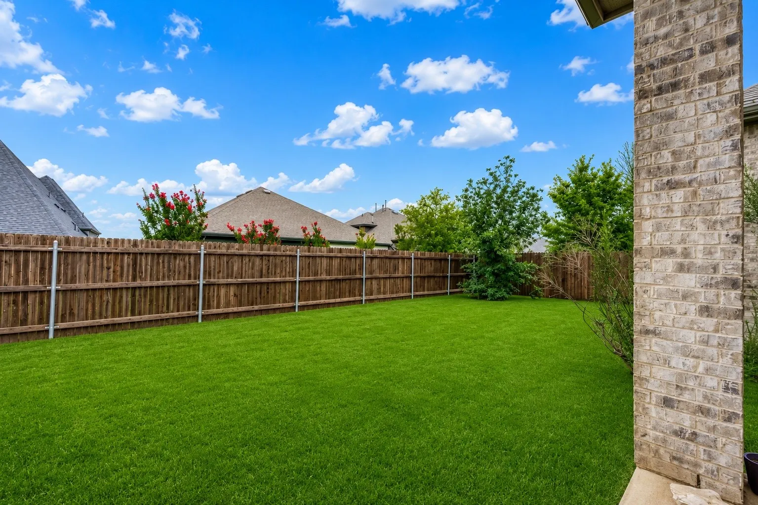 Spacious backyard featuring a lush lawn, privacy fencing, and mature landscaping
