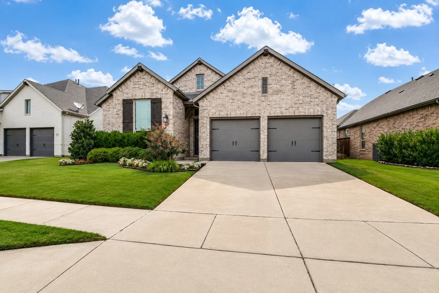 Brick facade with dark gray garage doors, a concrete driveway, and a manicured lawn