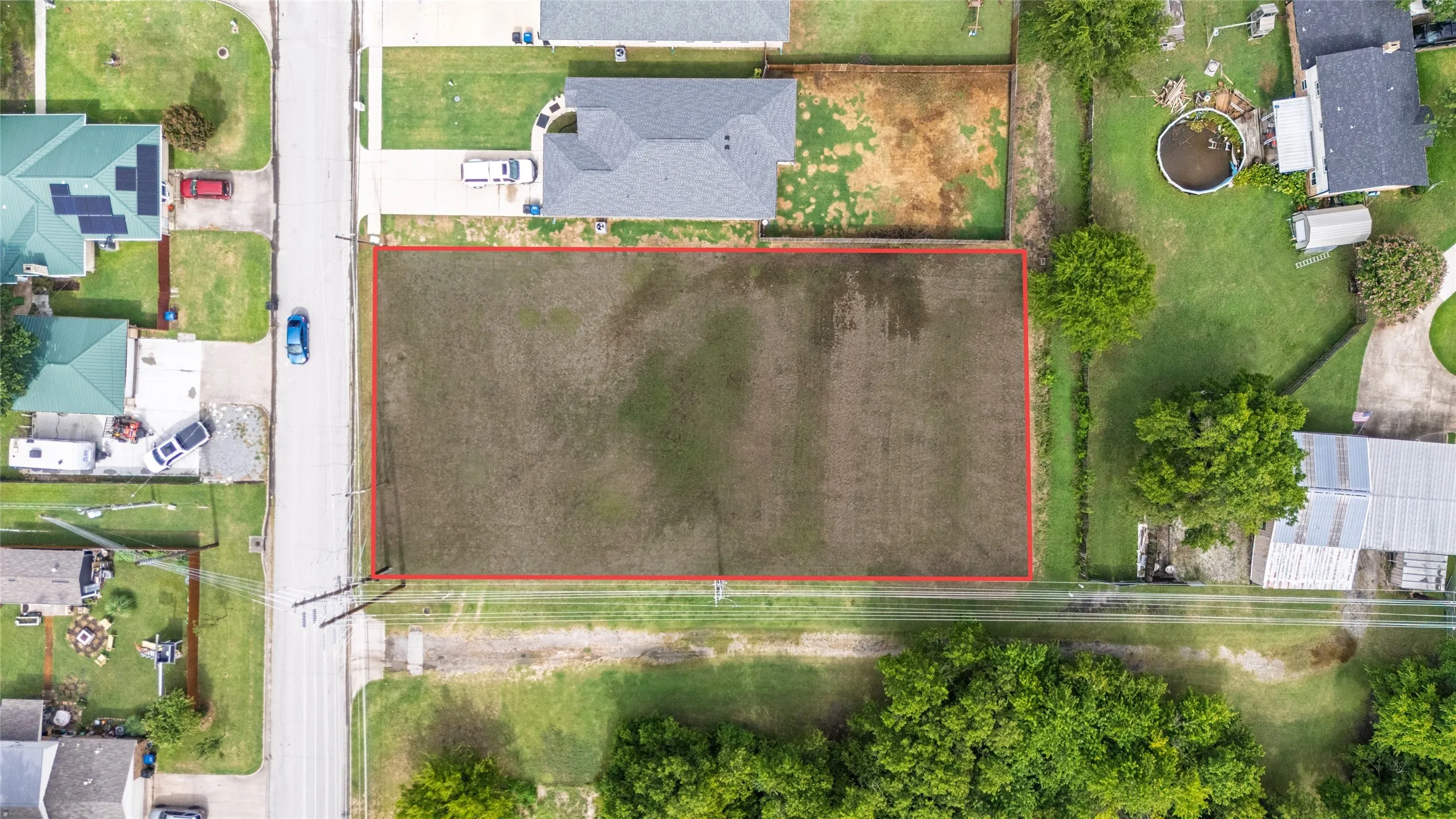 Level, undeveloped lot outlined in red, positioned along a paved road