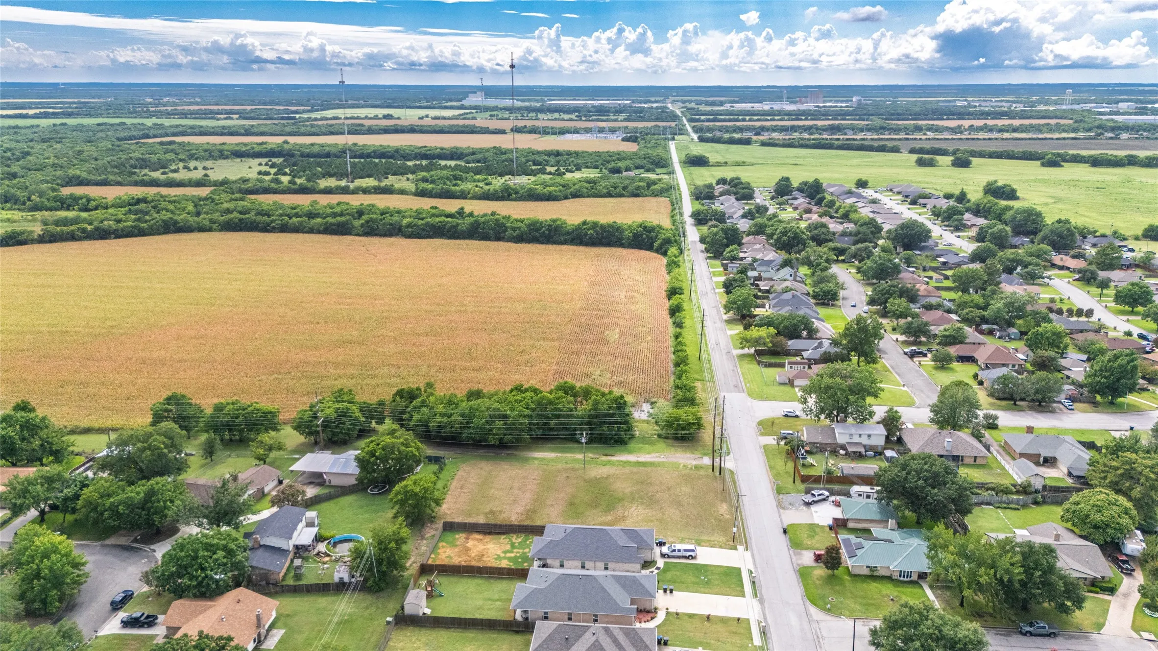 Expansive aerial showcasing a residential neighborhood bordered by agricultural fields and distant green spaces