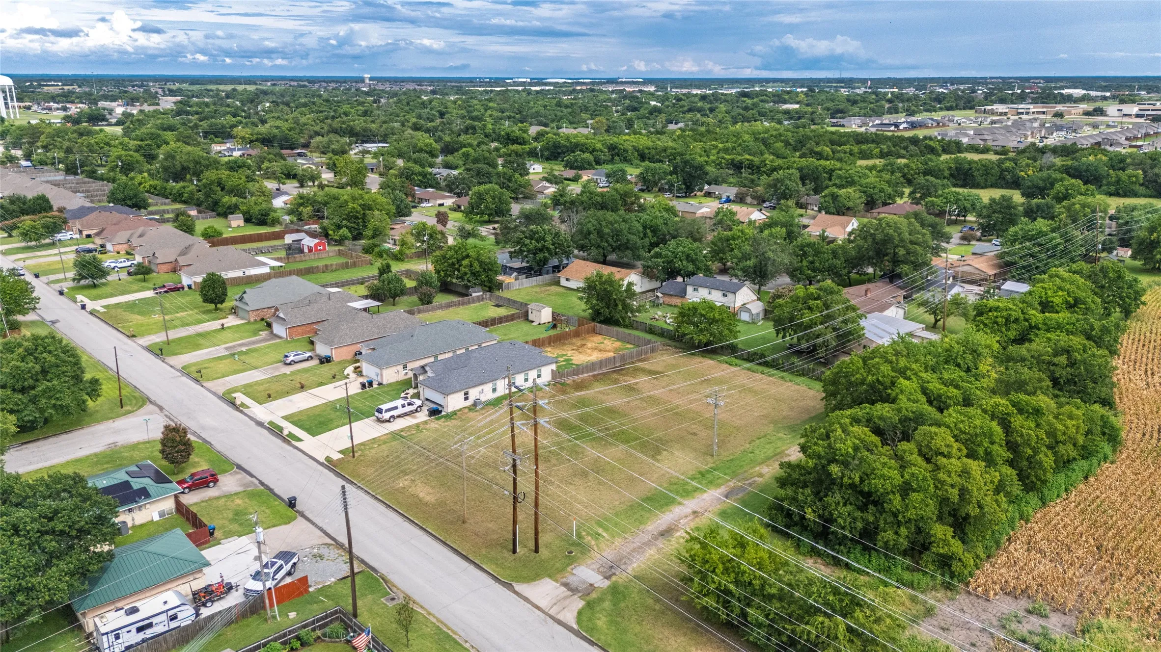 Expansive undeveloped lot with surrounding residential properties, bordering a cultivated field and mature tree line