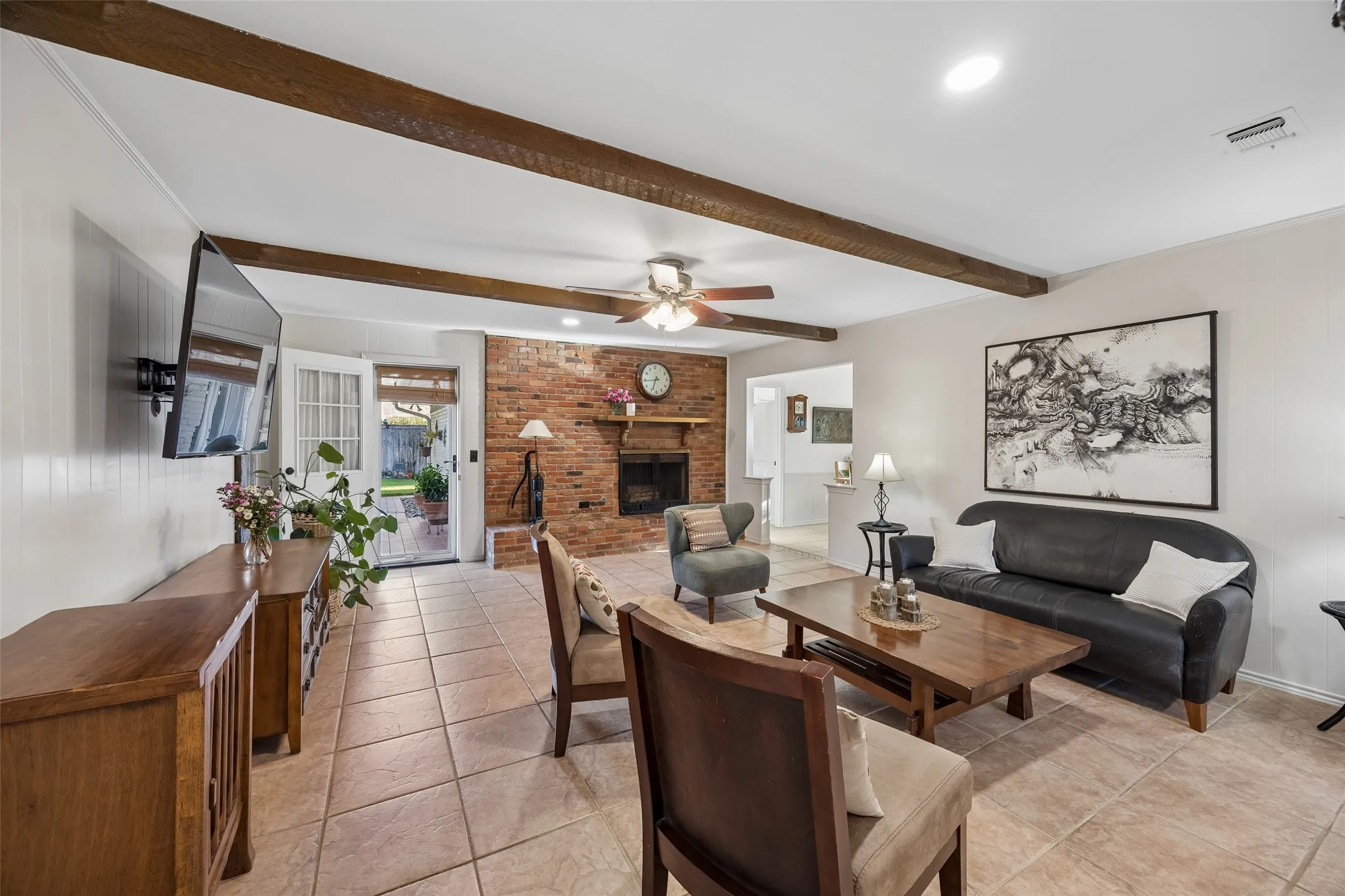 Spacious living area featuring exposed wood beams, a brick fireplace, and tiled flooring.