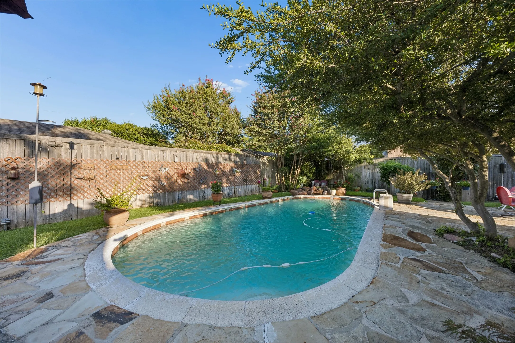 Outdoor swimming pool with flagstone patio surround, perimeter fencing, mature trees, and landscaping