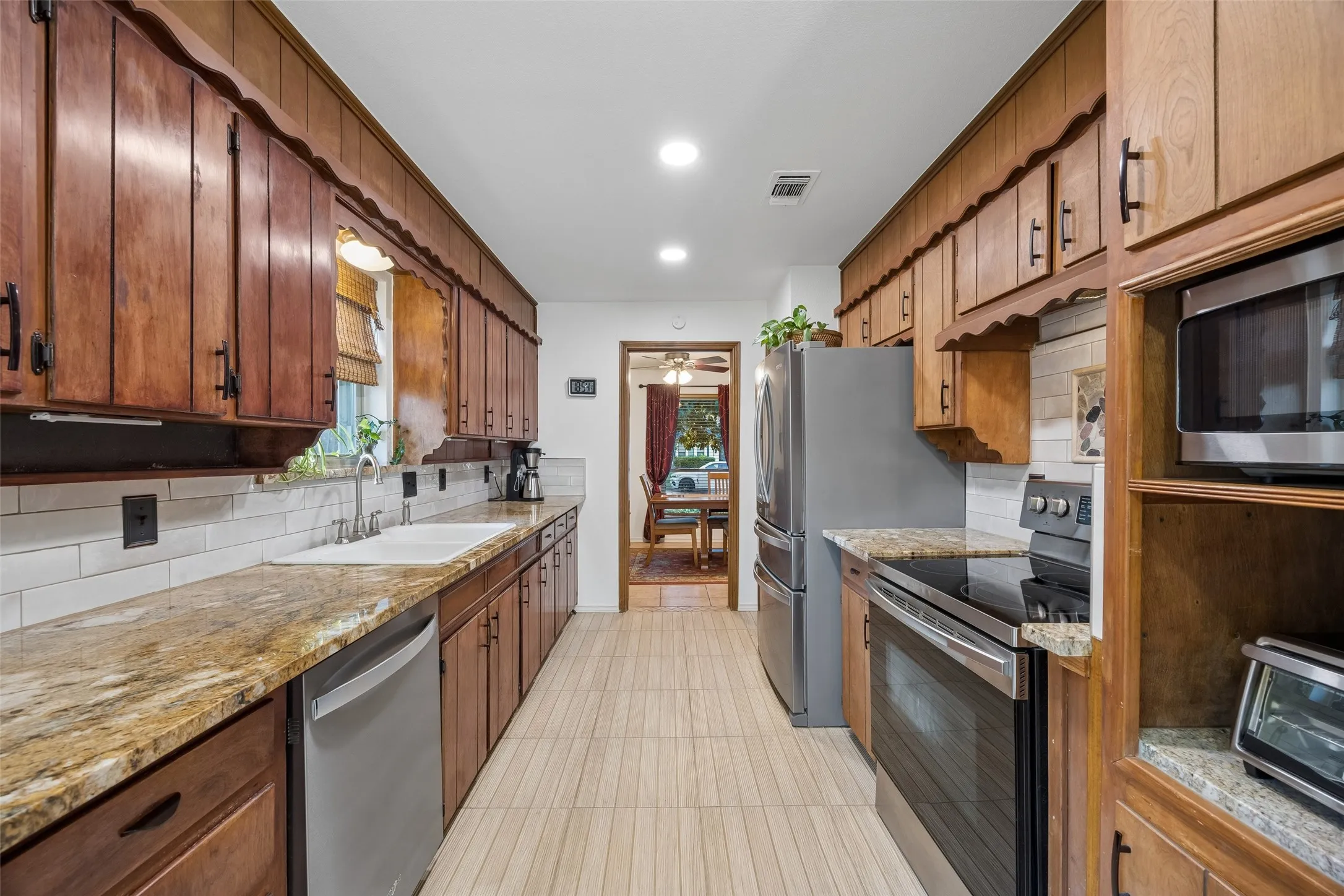 Galley kitchen featuring wood cabinetry, granite-finish countertops, and a white subway tile backsplash