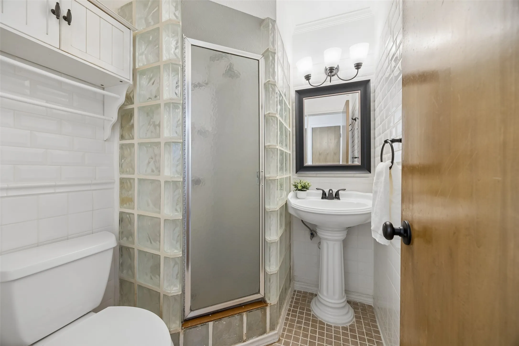 Bathroom featuring a glass block shower enclosure, white subway tile walls, and a pedestal sink with a framed mirror