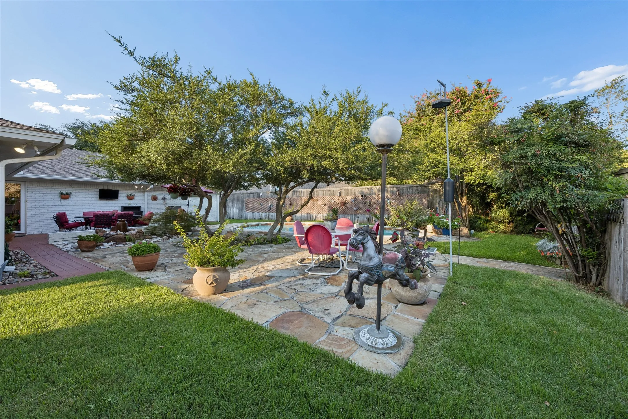 Expansive backyard featuring a stone patio, mature trees, manicured lawn, and a covered outdoor living area with a built-in entertainment system