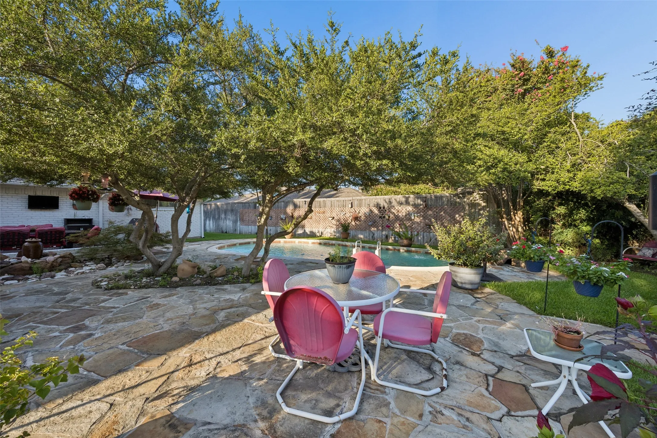 Expansive flagstone patio area with mature trees, a rectangular swimming pool, and a surrounding privacy fence