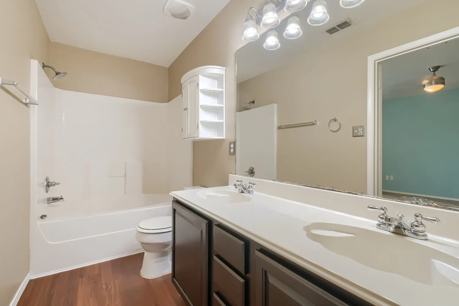 Bathroom featuring a double vanity with integrated sinks, wood-finish flooring, a white bathtub with shower, and a curved corner wall cabinet