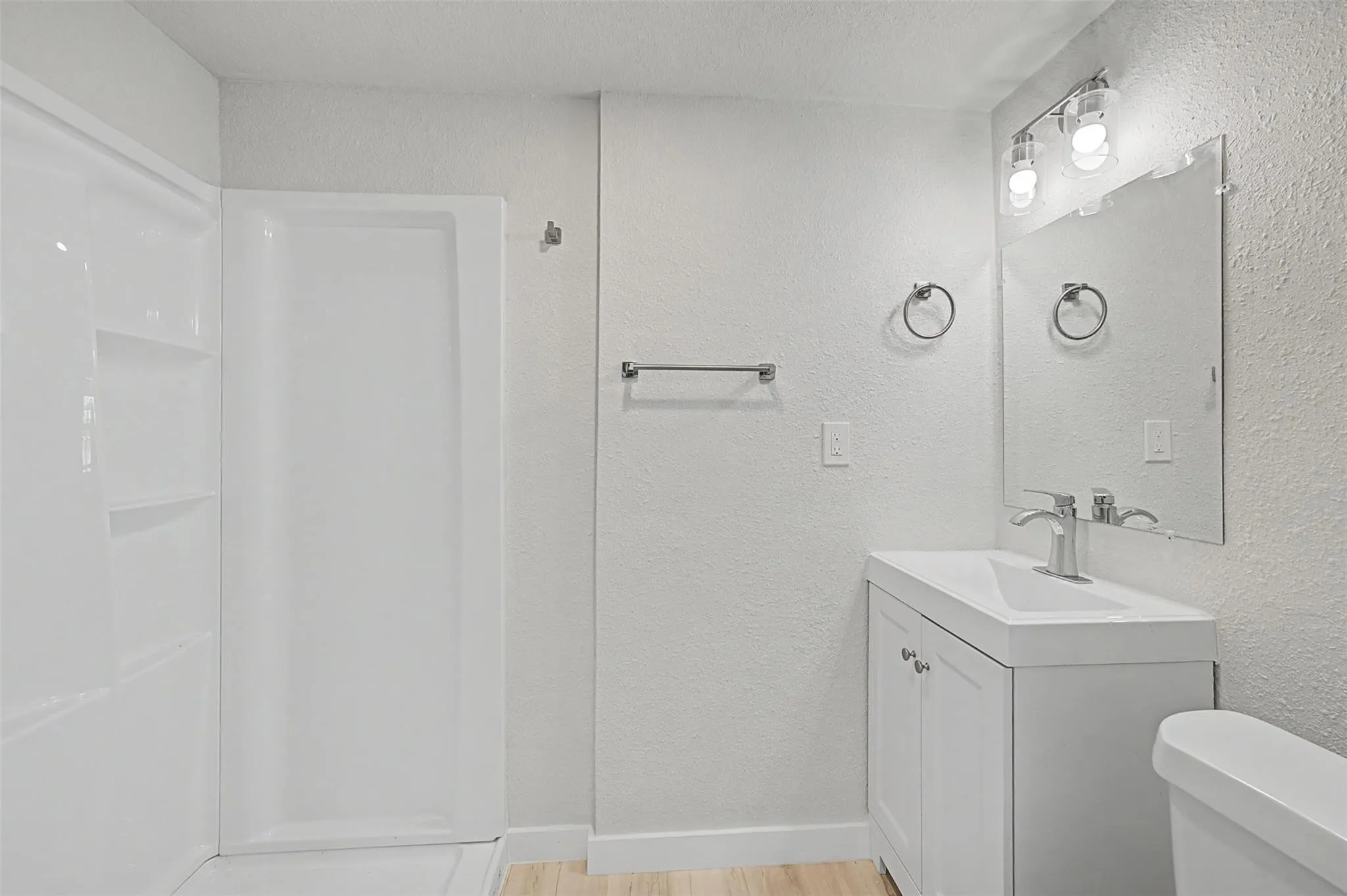Full bathroom featuring a walk-in shower with built-in shelving, a single vanity with a white basin sink and chrome faucet, and wood-finish flooring
