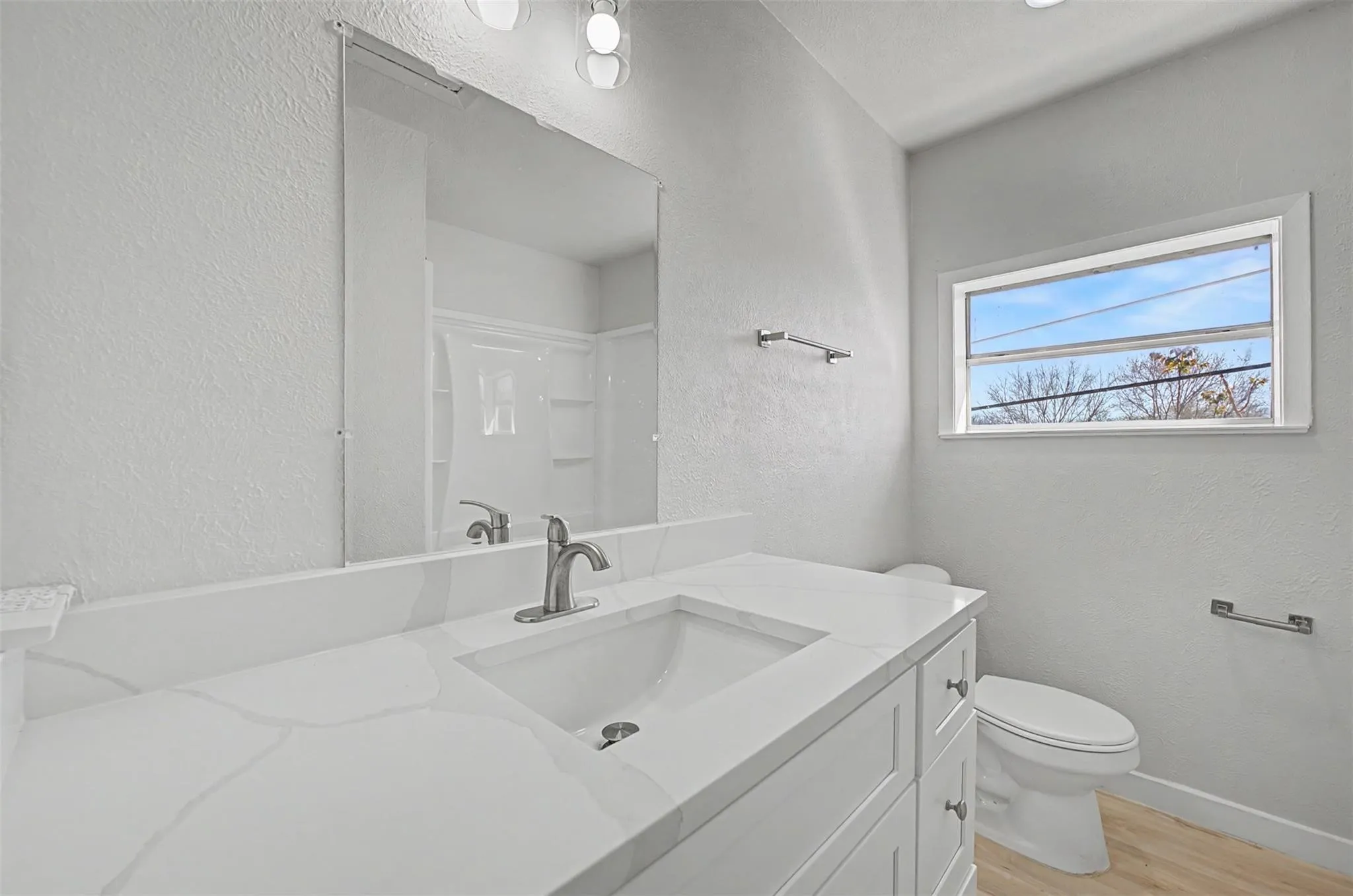 Bathroom featuring a white vanity with a built-in sink and light-colored countertop, brushed nickel faucet, large wall-mounted mirror, and a horizontal window