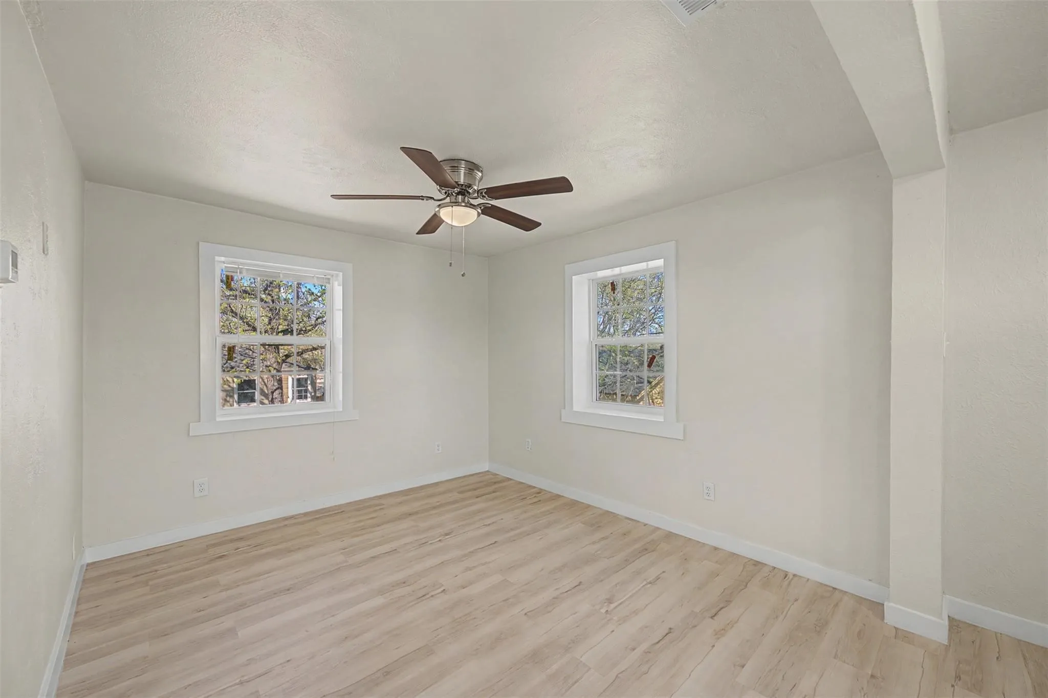 Bright interior room featuring light wood-finish flooring, white walls, and a ceiling fan with integrated lighting