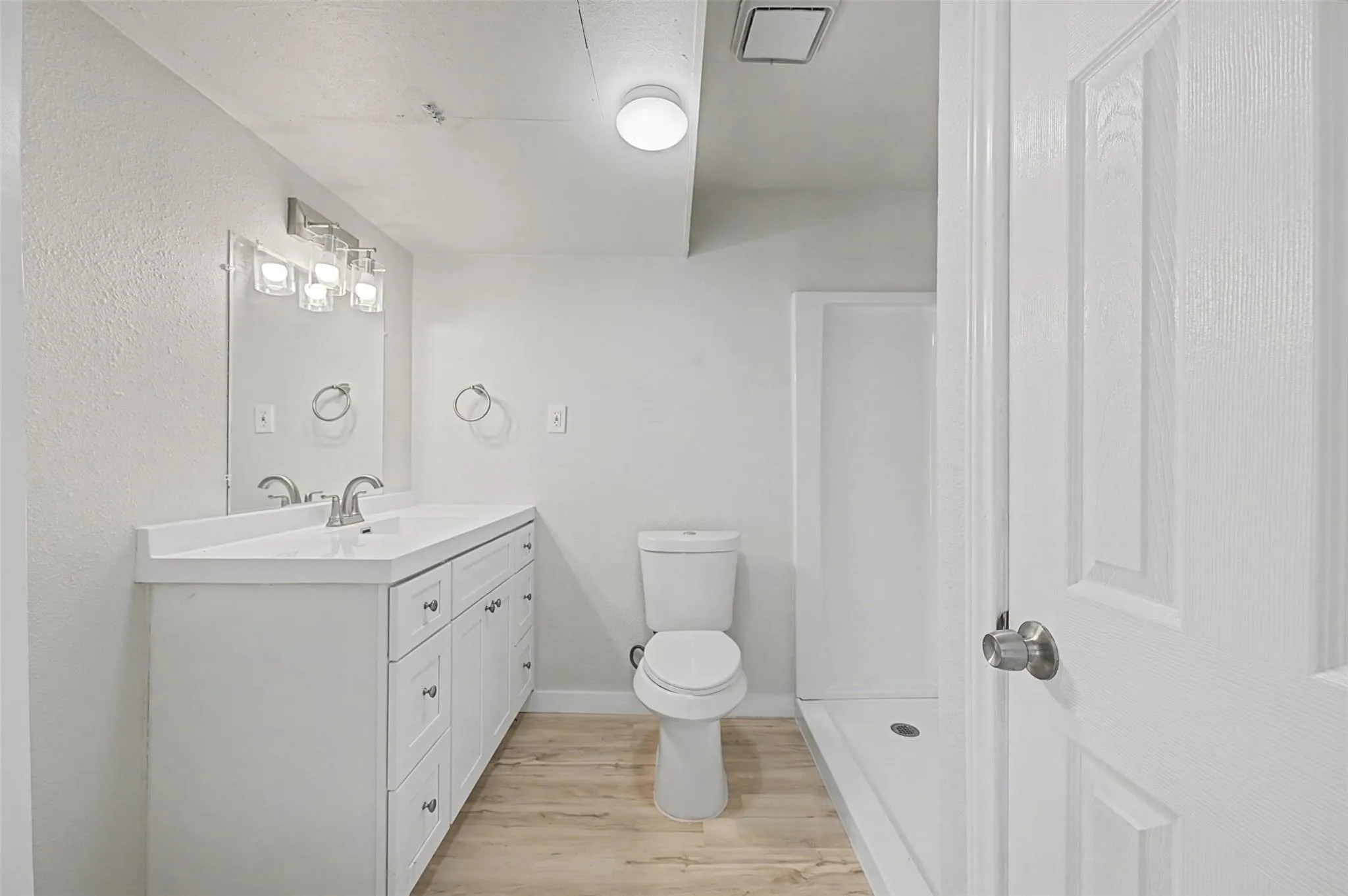 Bathroom featuring a single vanity with white cabinetry, a rectangular sink, and a light wood-finish floor