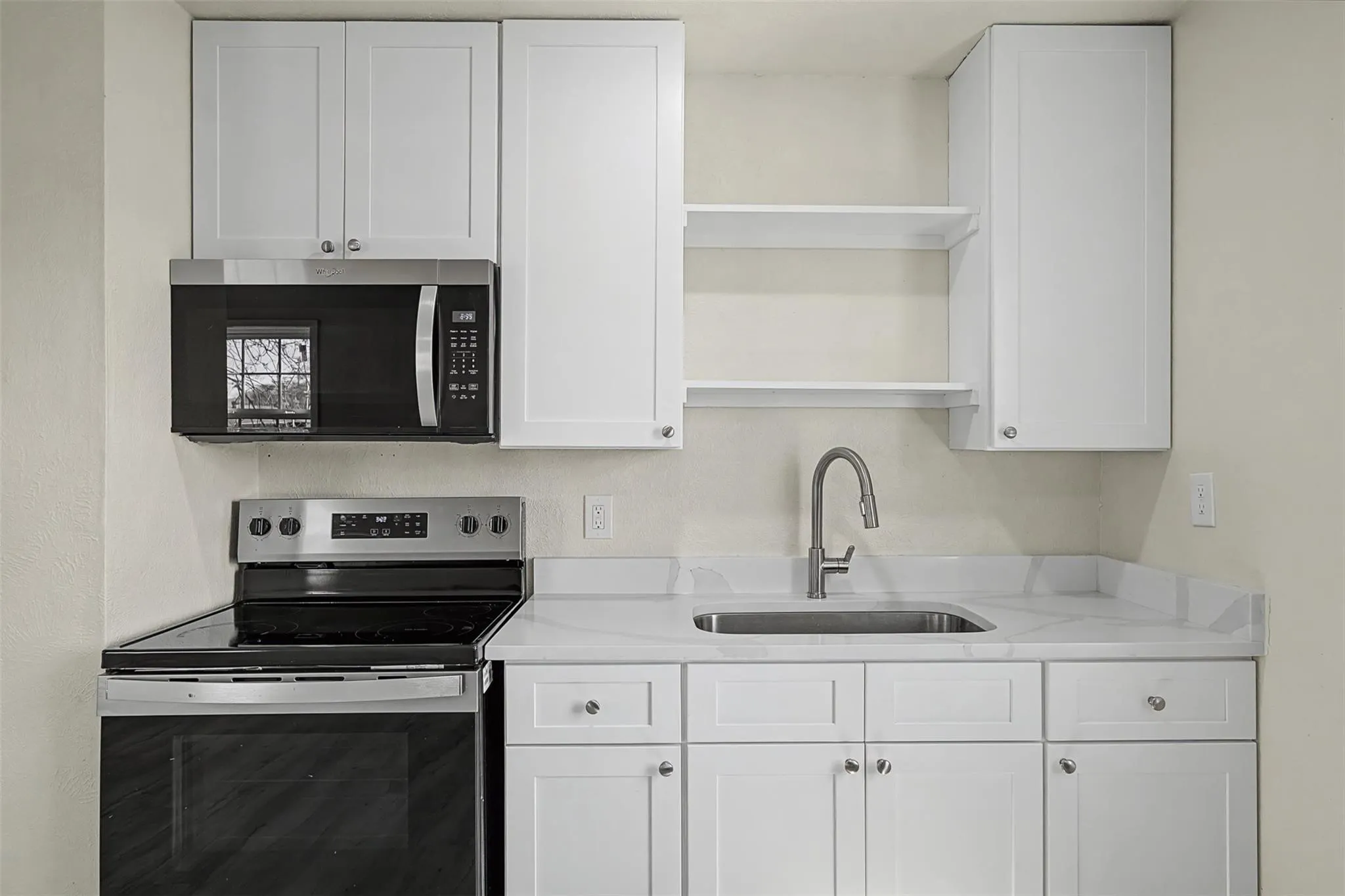 Kitchen featuring white shaker-style cabinetry, a stainless steel sink with a gooseneck faucet, white stone countertops, and a black over-the-range microwave