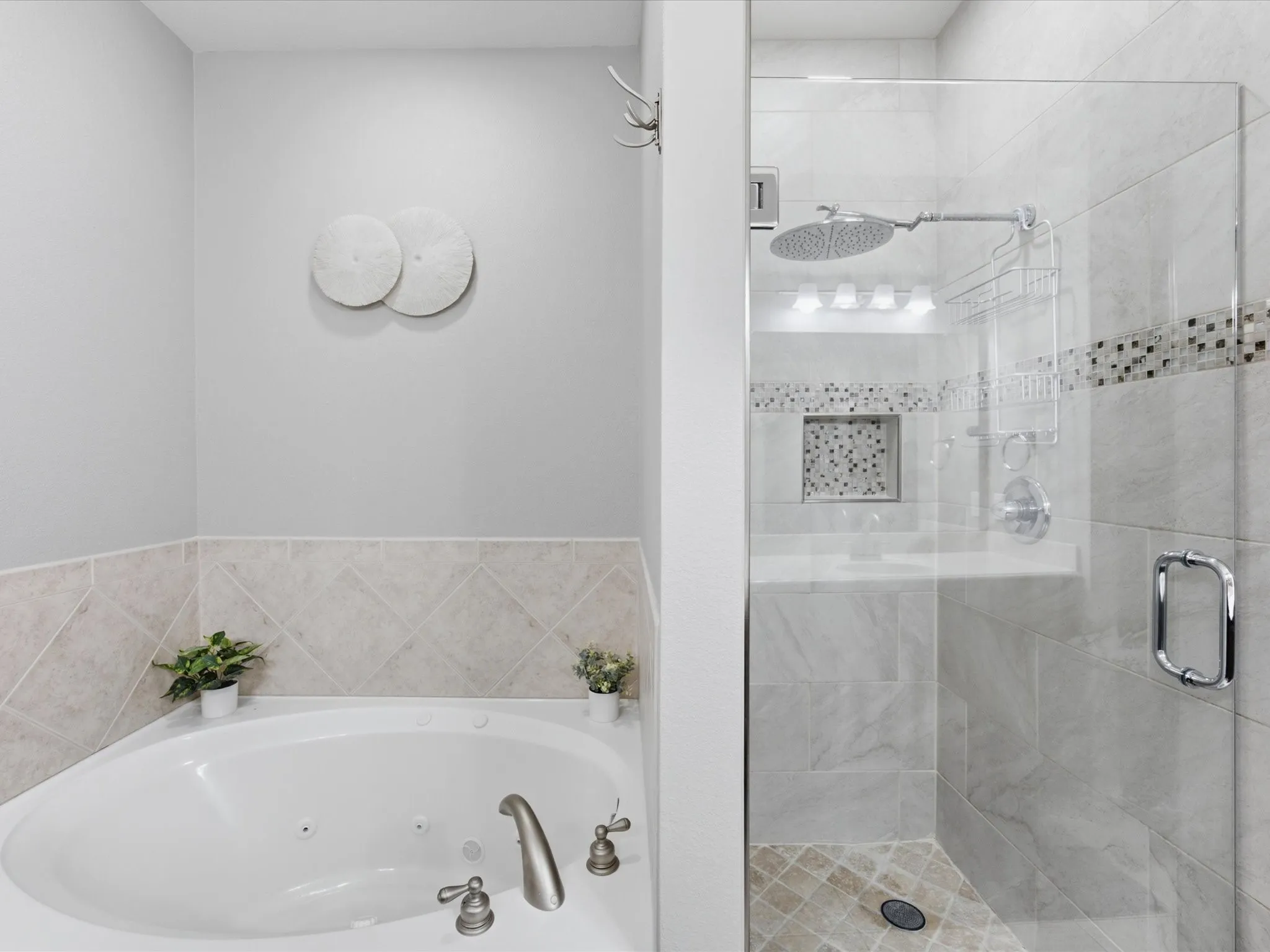 Corner jetted tub with brushed nickel fixtures, complemented by a glass-enclosed shower featuring a rain showerhead, mosaic tile accent, and a built-in shower niche