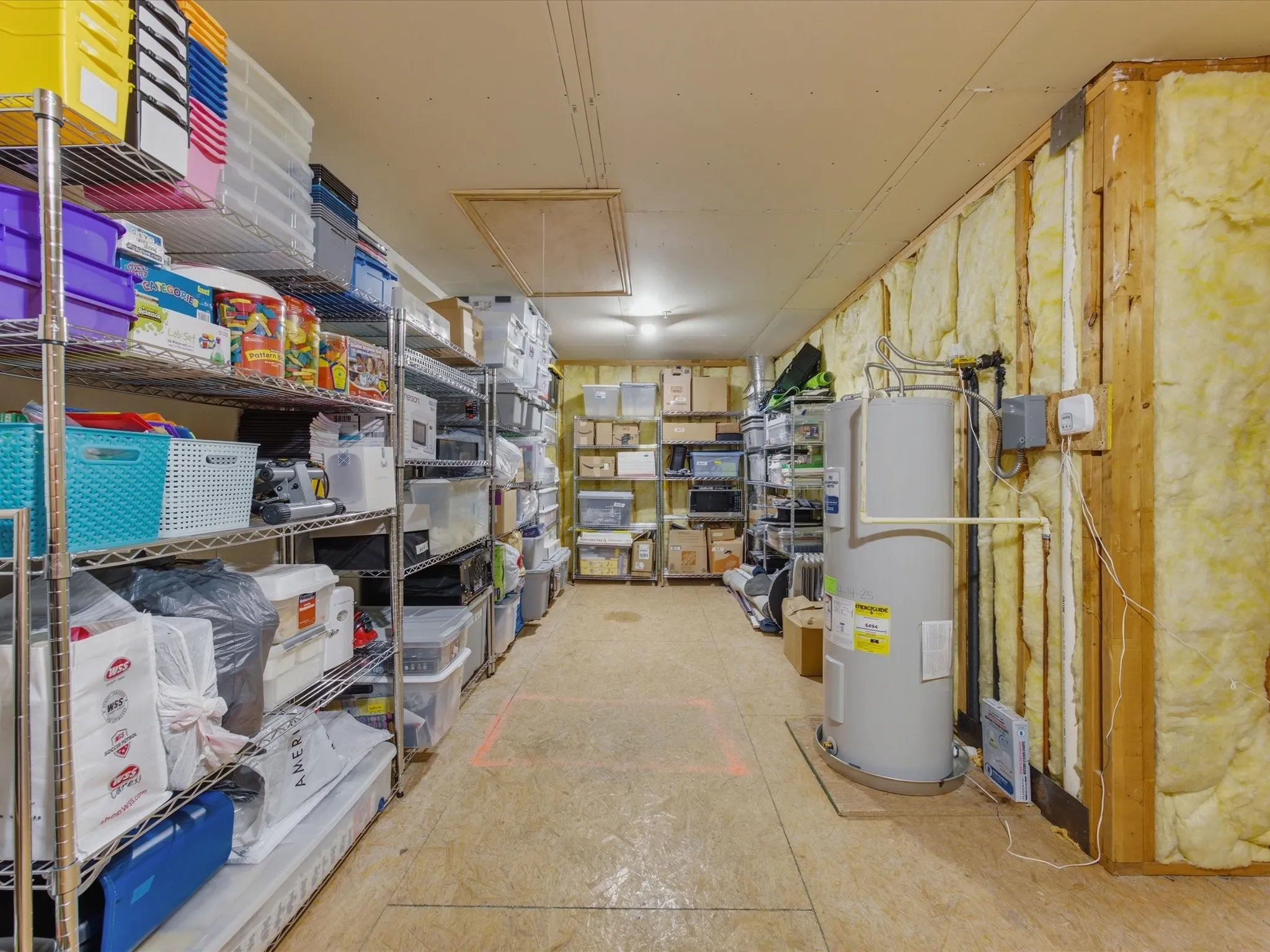Spacious upstairs storage area featuring metal shelving units, a water heater, and exposed insulation
