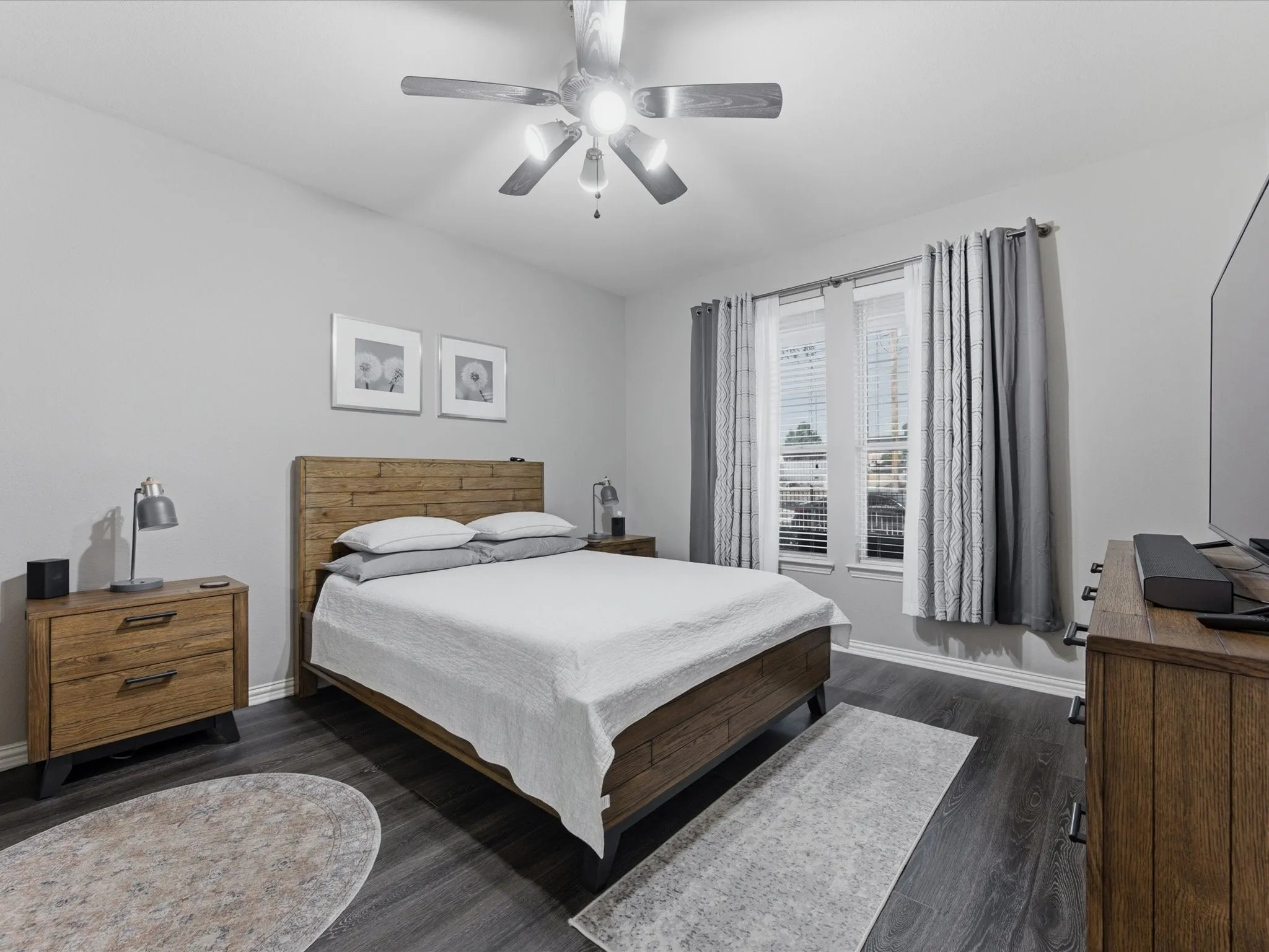 Primary Bedroom featuring light gray walls, dark wood-finish flooring, a ceiling fan with integrated lighting, and a large window with blinds and curtains