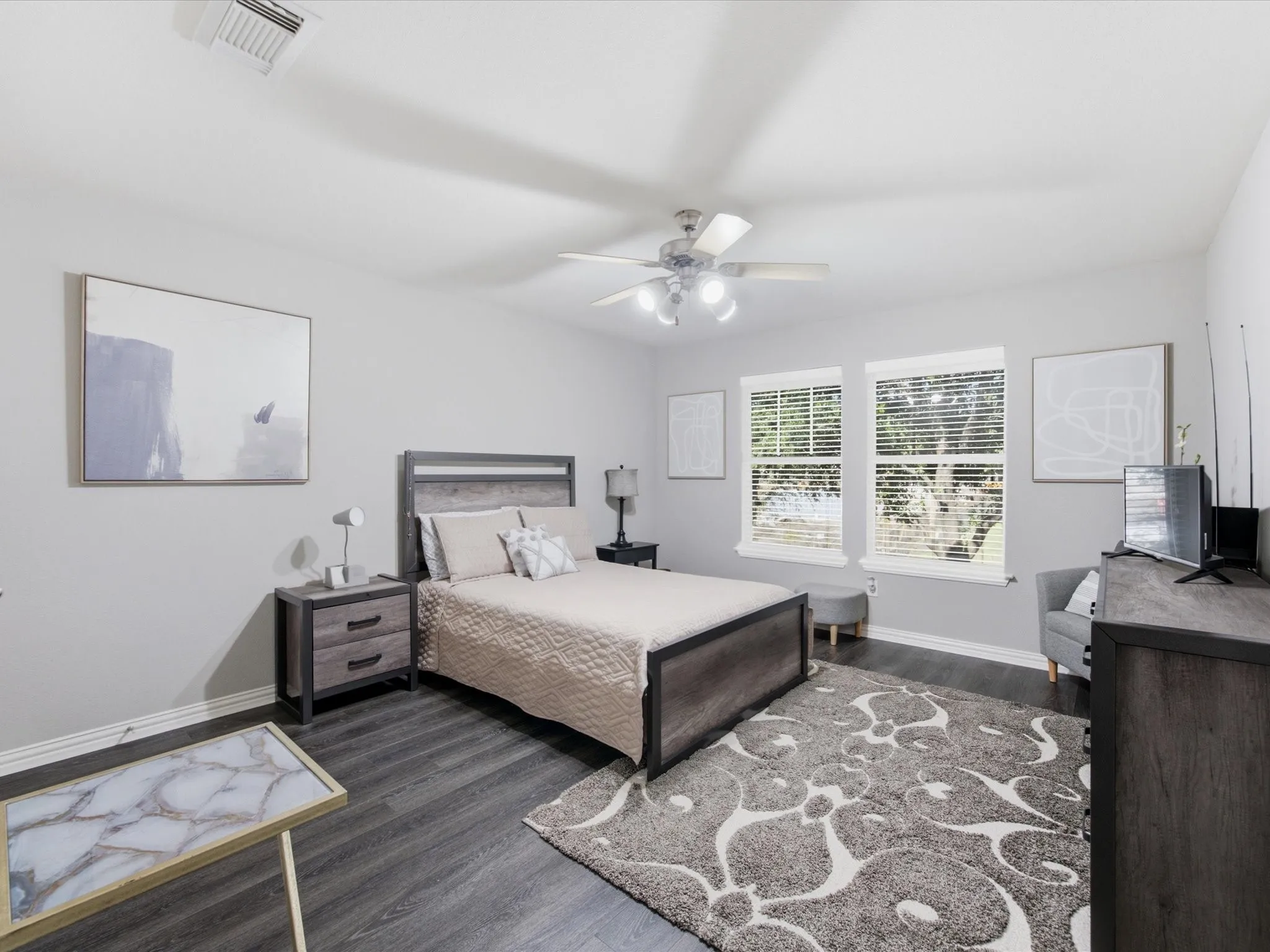 Spacious room featuring wood-finish flooring, two large windows, a ceiling fan with integrated lighting, and neutral wall tones