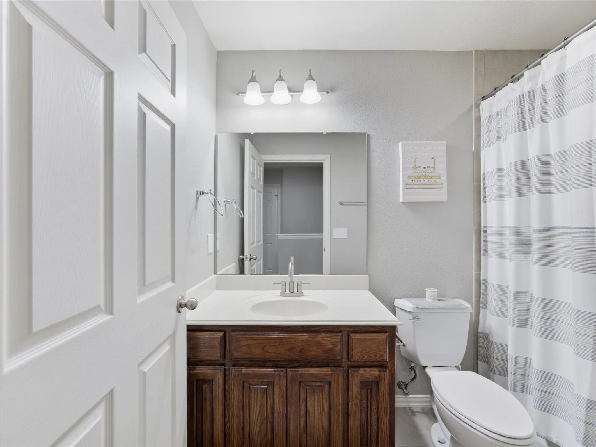 Bathroom featuring a wood-finish vanity with an integrated sink, a white countertop, and a vanity mirror with sconce lighting