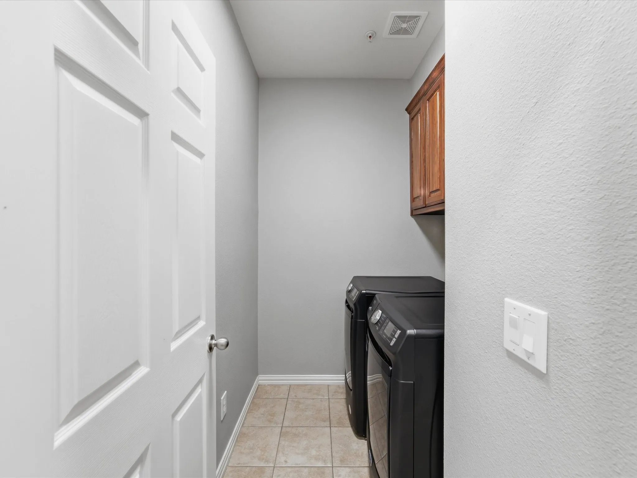 Laundry area featuring neutral-toned tile flooring, light gray walls, and a wood-finish upper cabinet