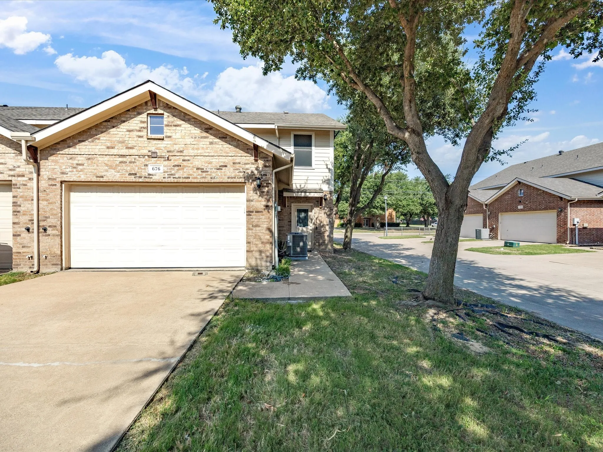 Brick exterior with an attached garage, paved driveway, and established trees