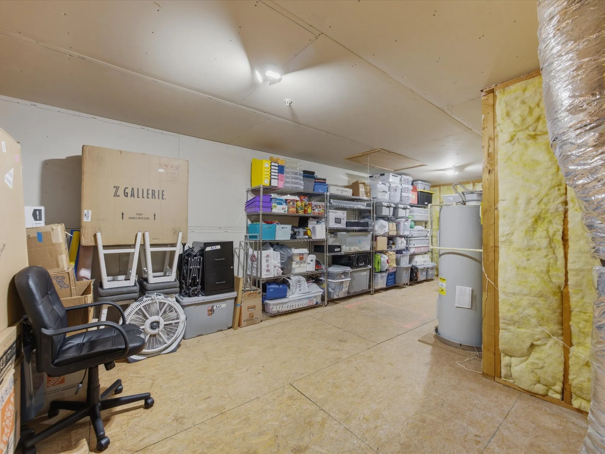 Spacious upstairs storage area featuring metal shelving units, a water heater, and exposed insulation