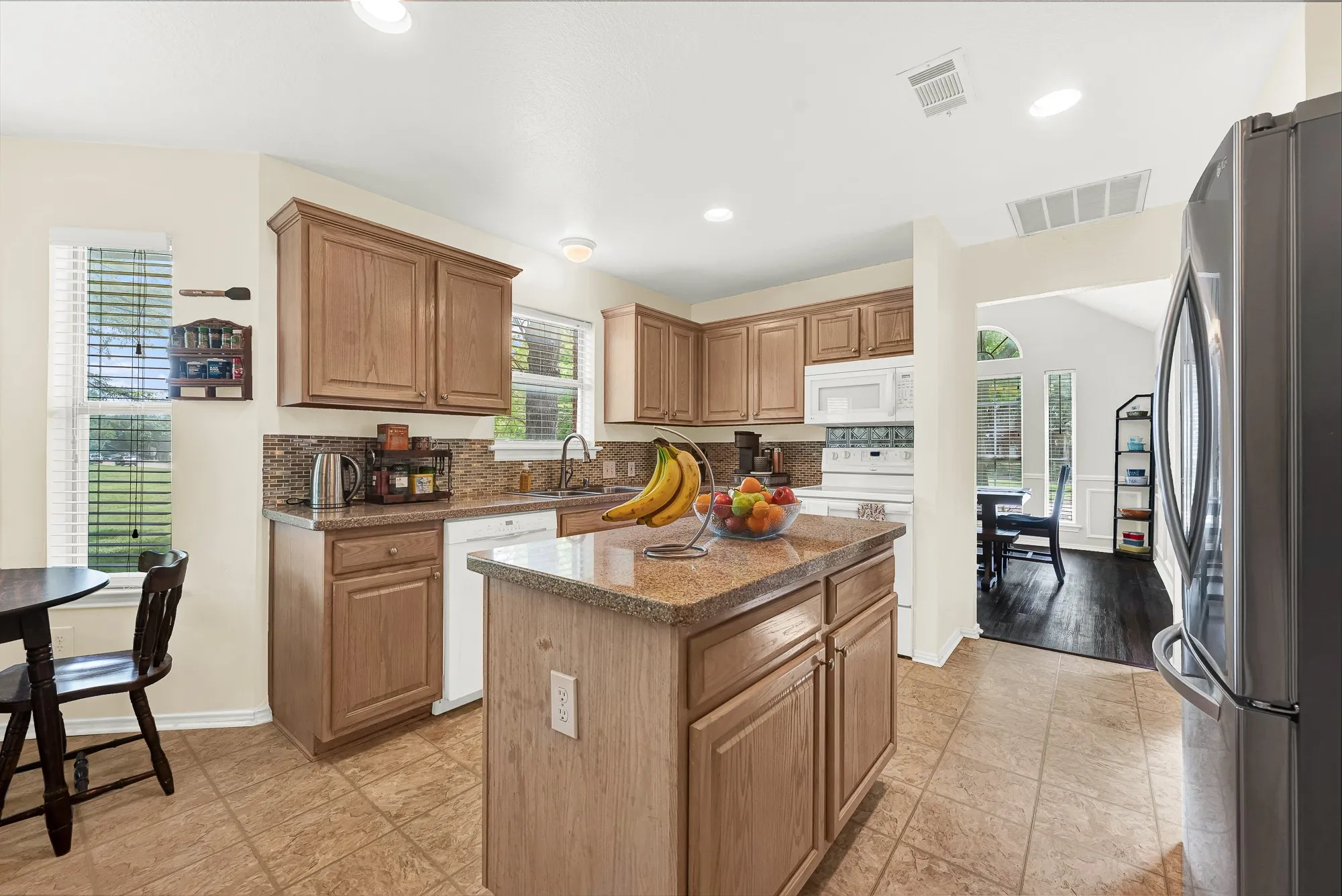 Kitchen featuring an island with stone-finish countertop, wood cabinetry, tile flooring, and a white built-in microwave and range