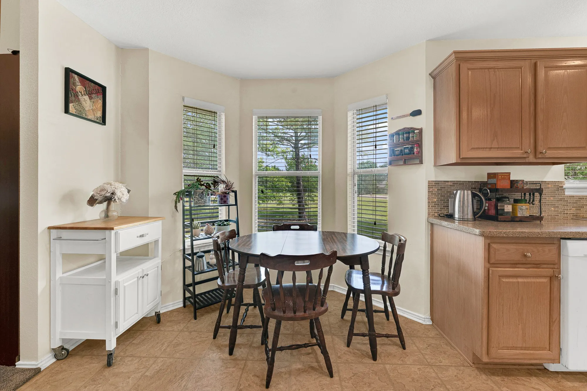 Bay window dining area with natural light, light wood cabinetry, tiled flooring, and a mosaic tile backsplash