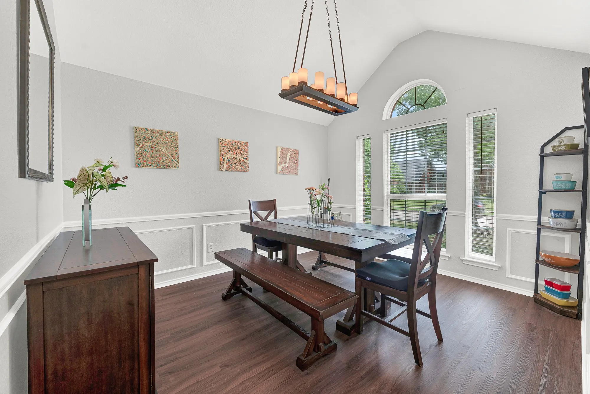 Formal dining area featuring a vaulted ceiling with an arched window, wood-finish flooring, and wainscoting