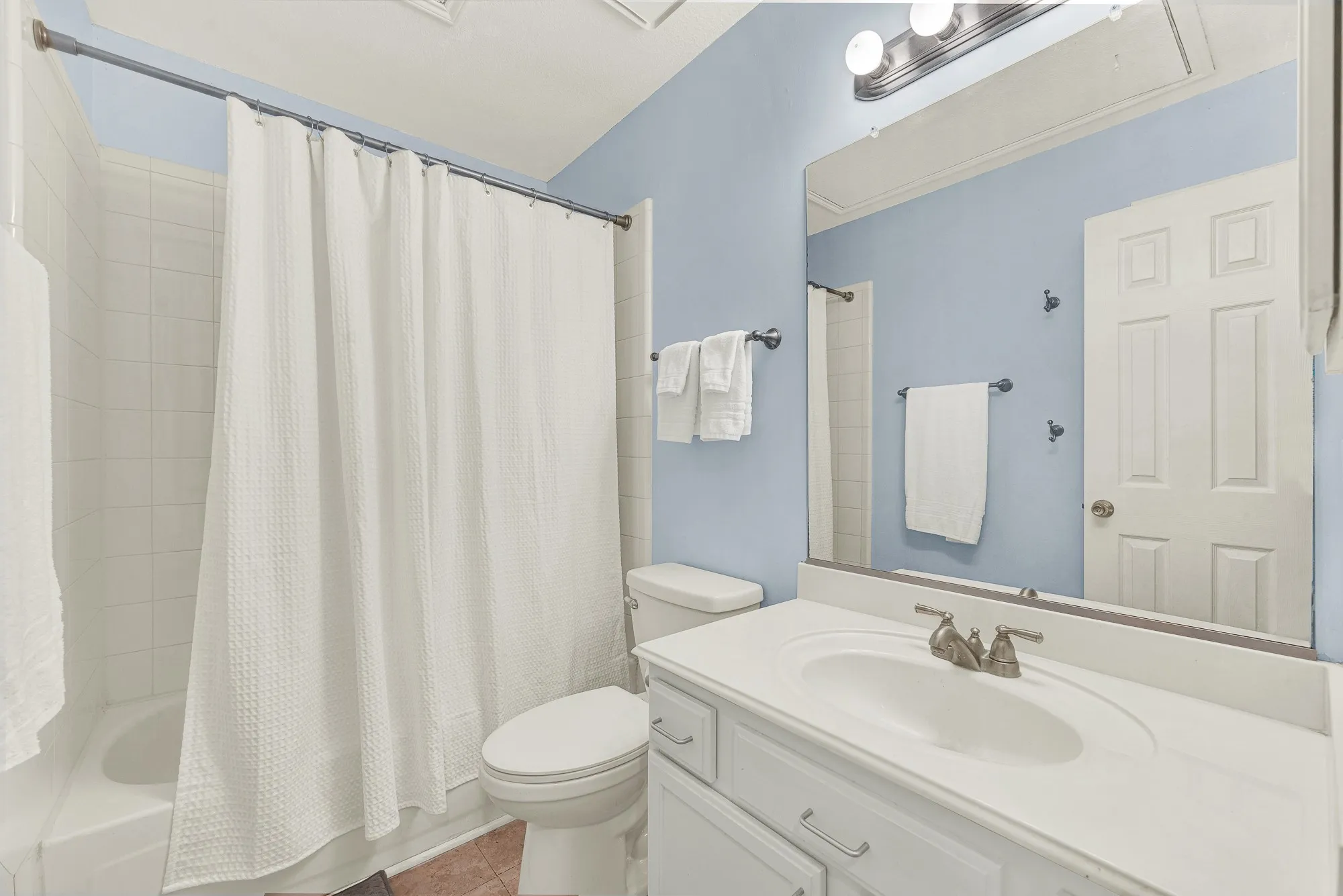 Bathroom featuring a single vanity with a white countertop and undermount sink, brushed nickel faucet, and a large wall-mounted mirror