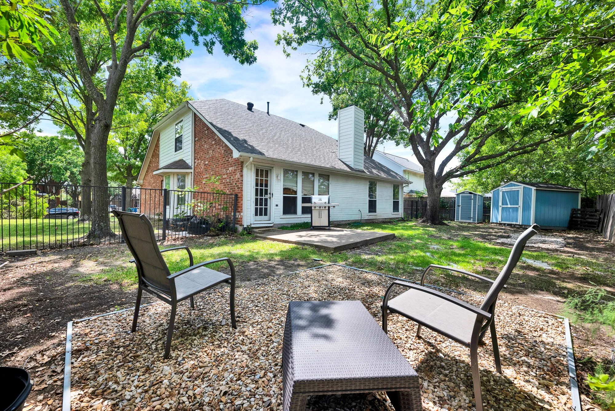 Spacious backyard featuring mature trees, a concrete patio, and a black iron fence, the seller used to have a greenhouse in this spot.