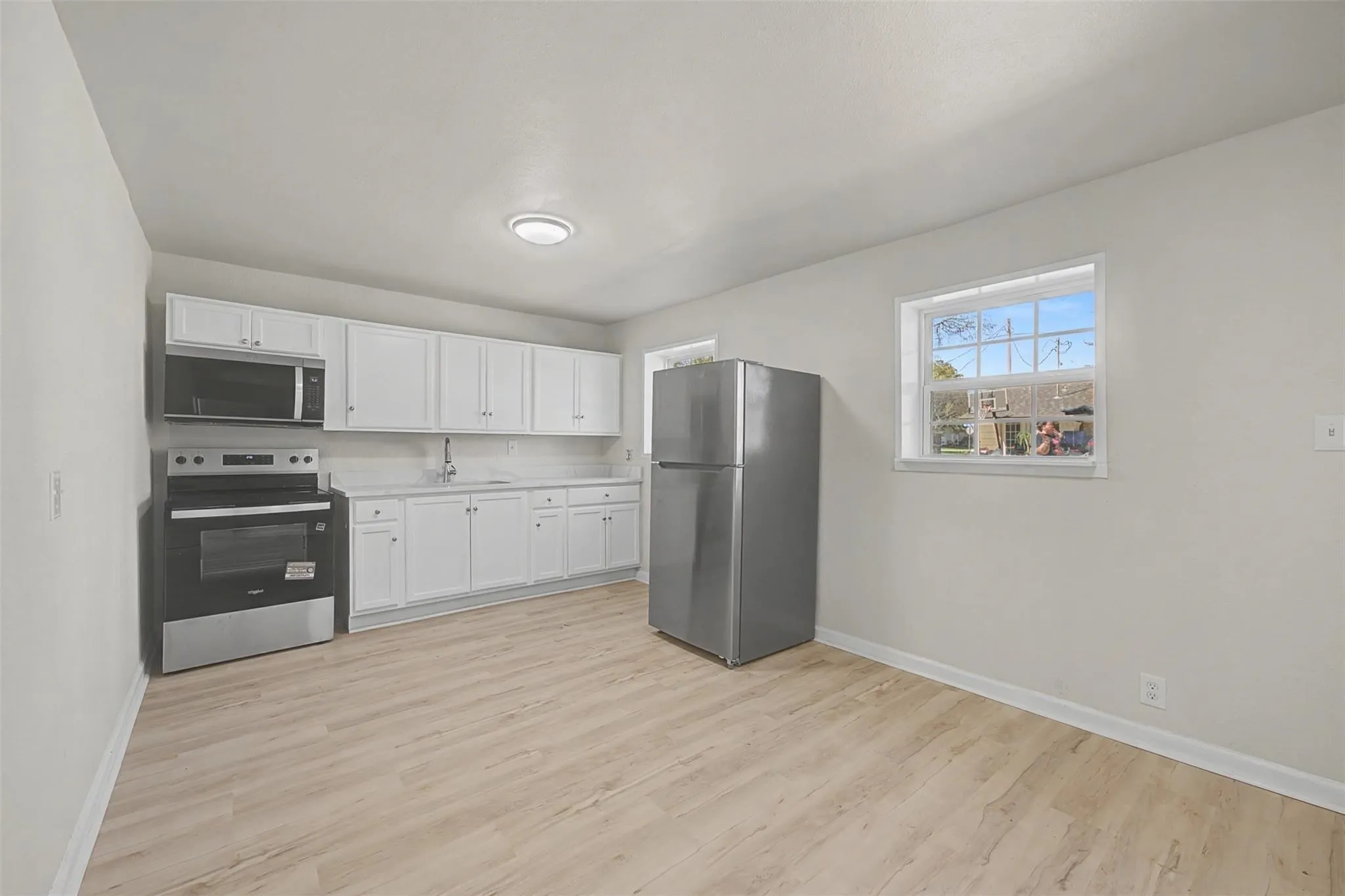 Kitchen featuring white cabinetry, light countertops, wood-finish flooring, a stainless steel refrigerator, and a stainless steel oven with an overhead microwave