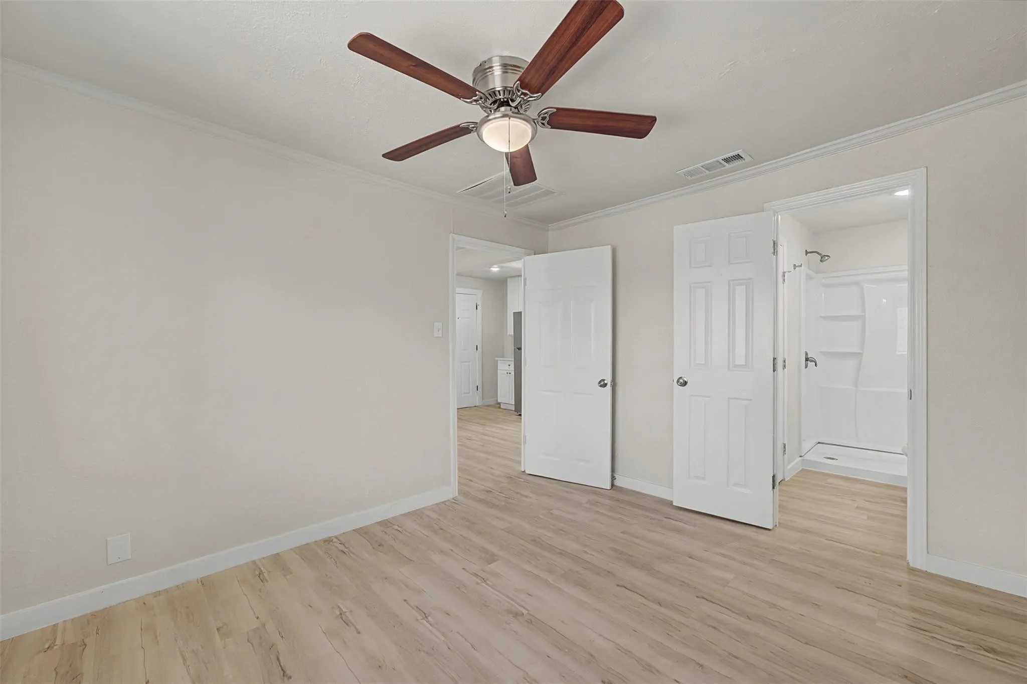 Light wood-finish flooring extending into an en-suite bathroom featuring a walk-in shower with a white surround