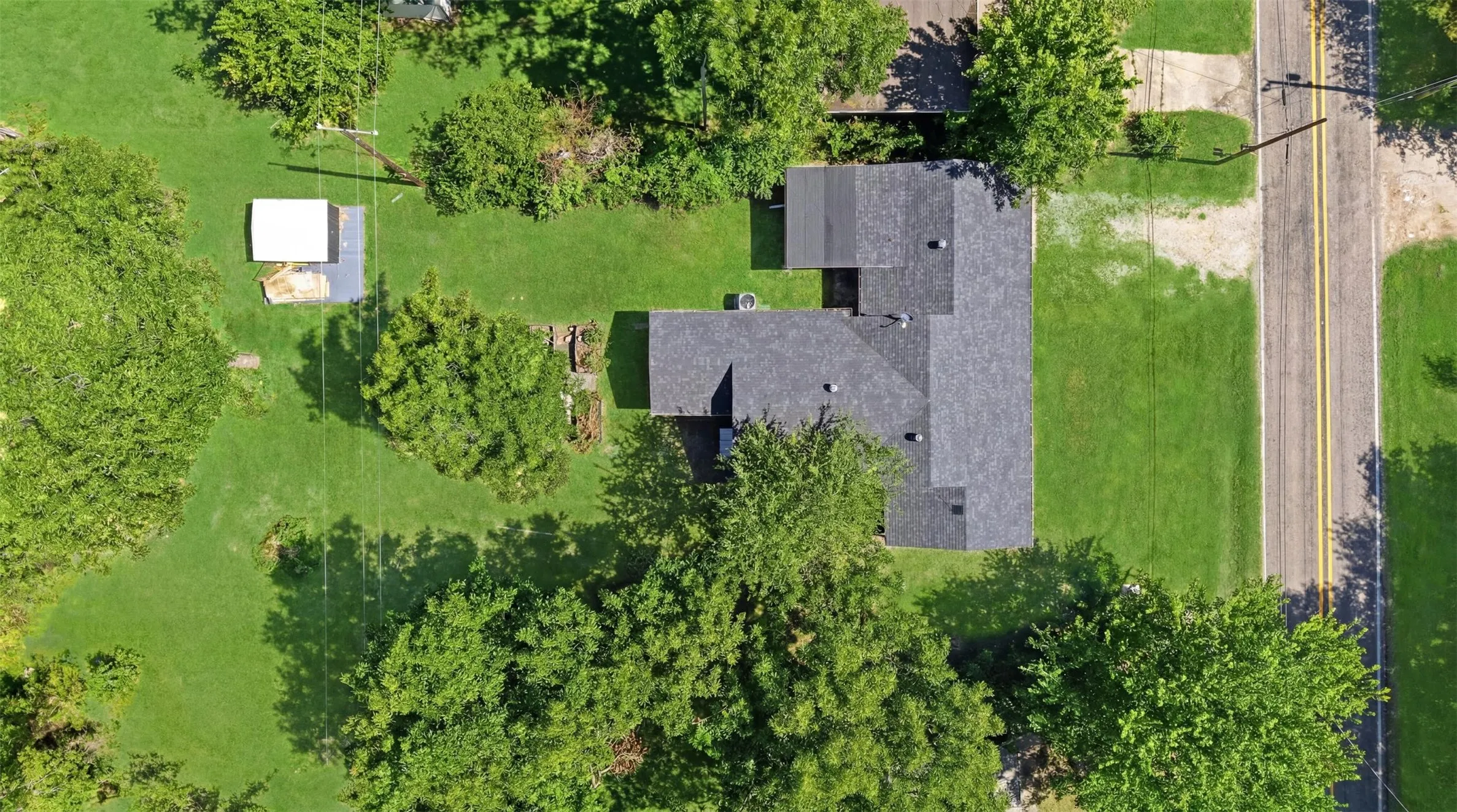 Aerial perspective showcasing a property with a dark shingle roof, surrounded by mature trees and verdant lawns