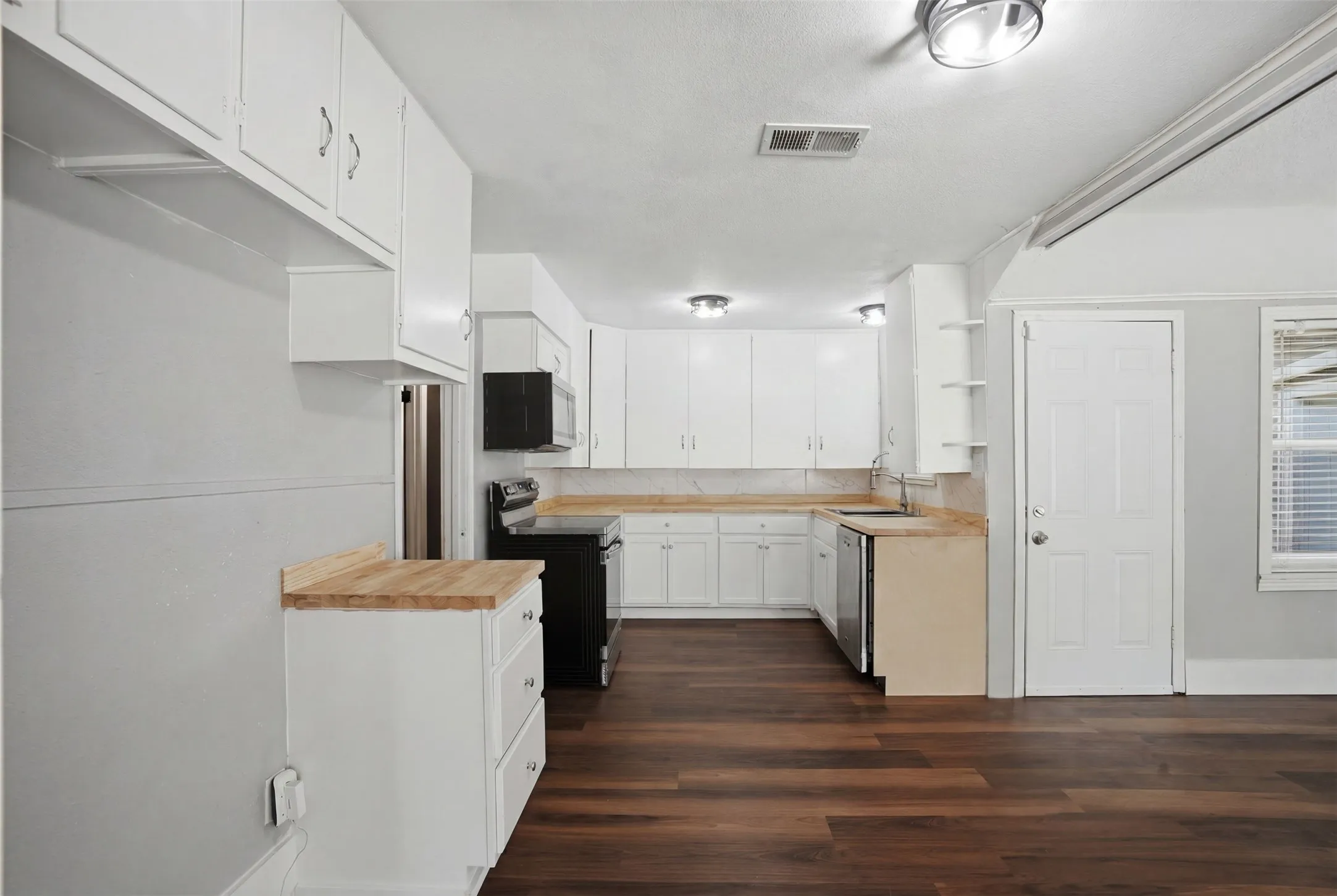 Kitchen featuring white cabinetry, wood-finish flooring, a stainless steel dishwasher, black range, and light-toned countertops