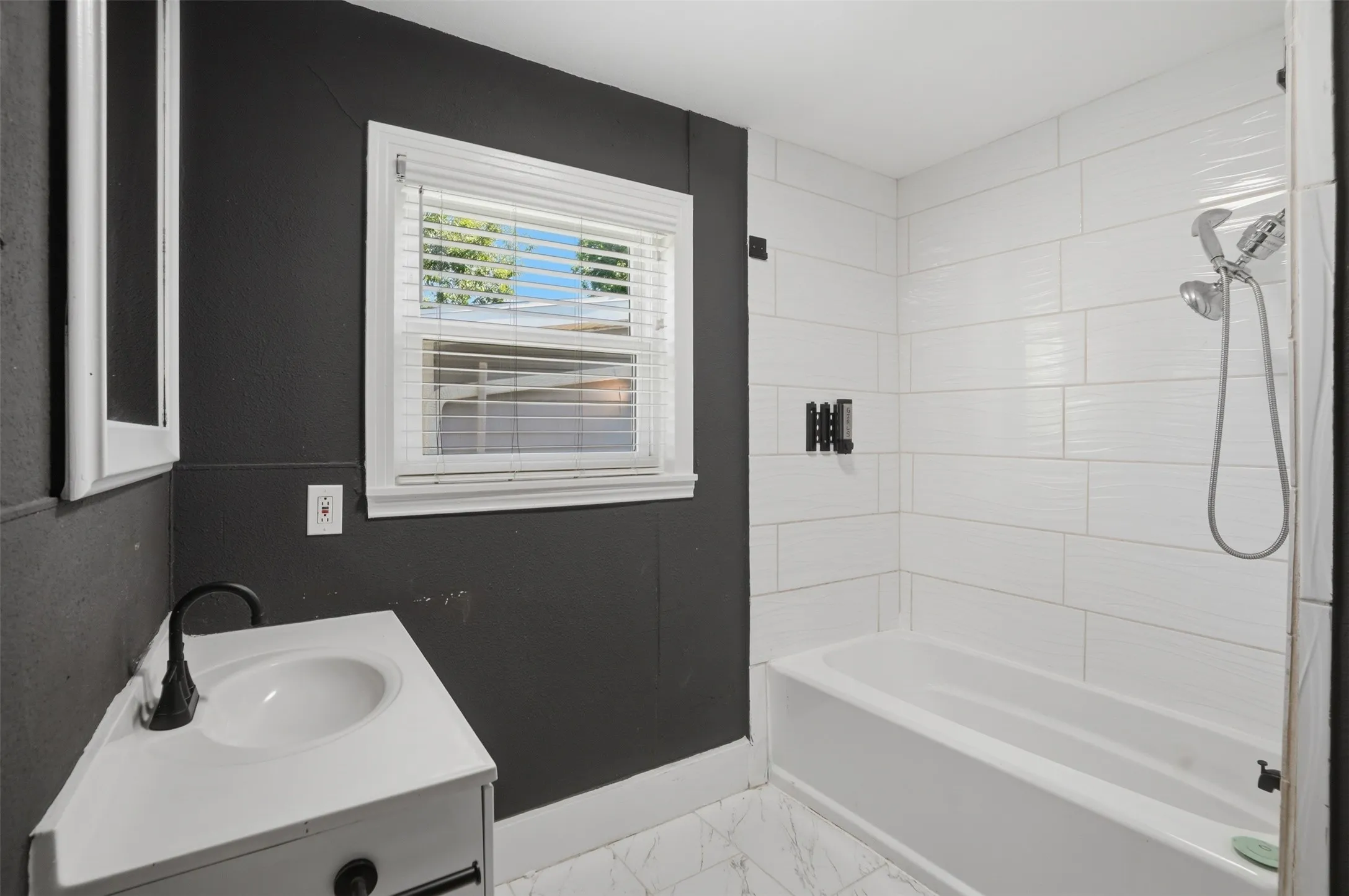 Bathroom featuring a white bathtub, white subway tile surround, white vanity with integrated sink, and matte black fixtures
