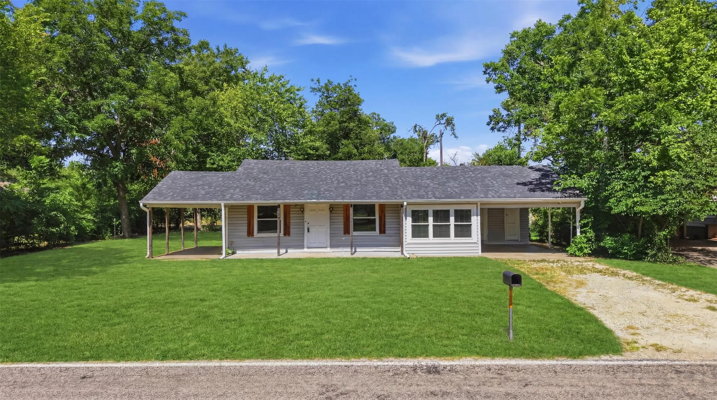 Ranch-style exterior with gray siding, a dark gray shingle roof, and a covered front porch featuring white support columns